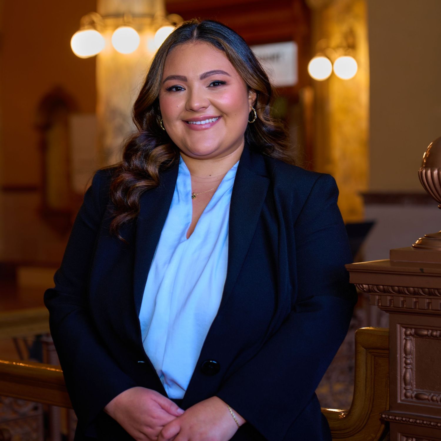 Professional in a navy blazer and light blue blouse poses in an elegant indoor setting.