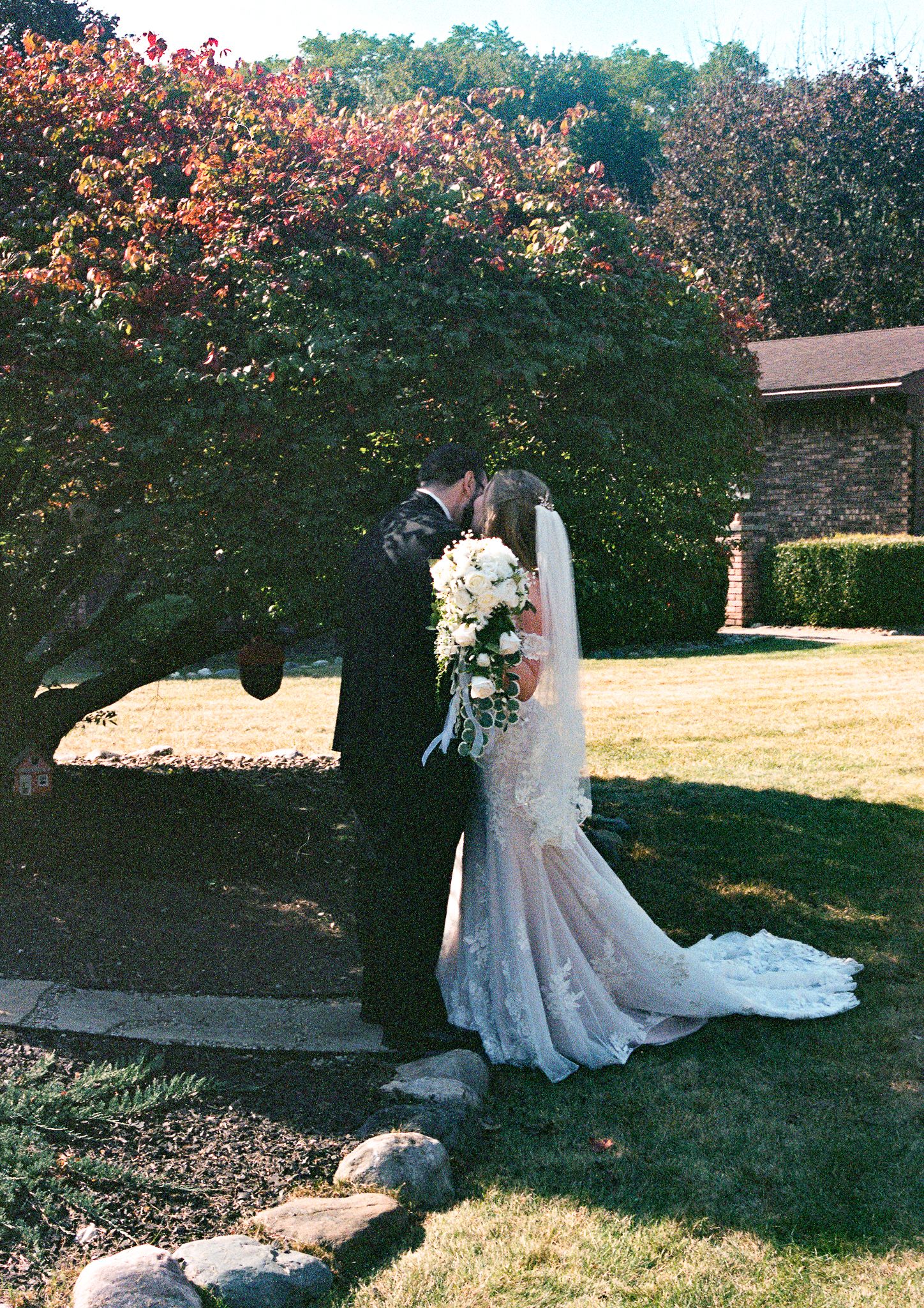 A beautiful white wedding dress with lace details and flowing train laid out on green grass in an outdoor garden setting.
