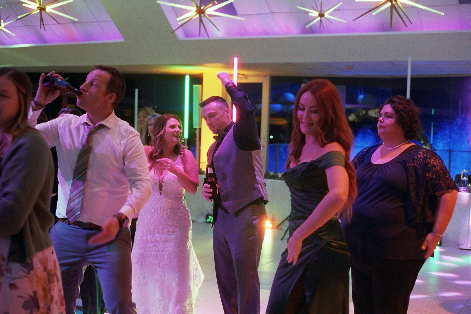 People dancing and socializing at an evening event with purple lighting and a colorful dance floor.