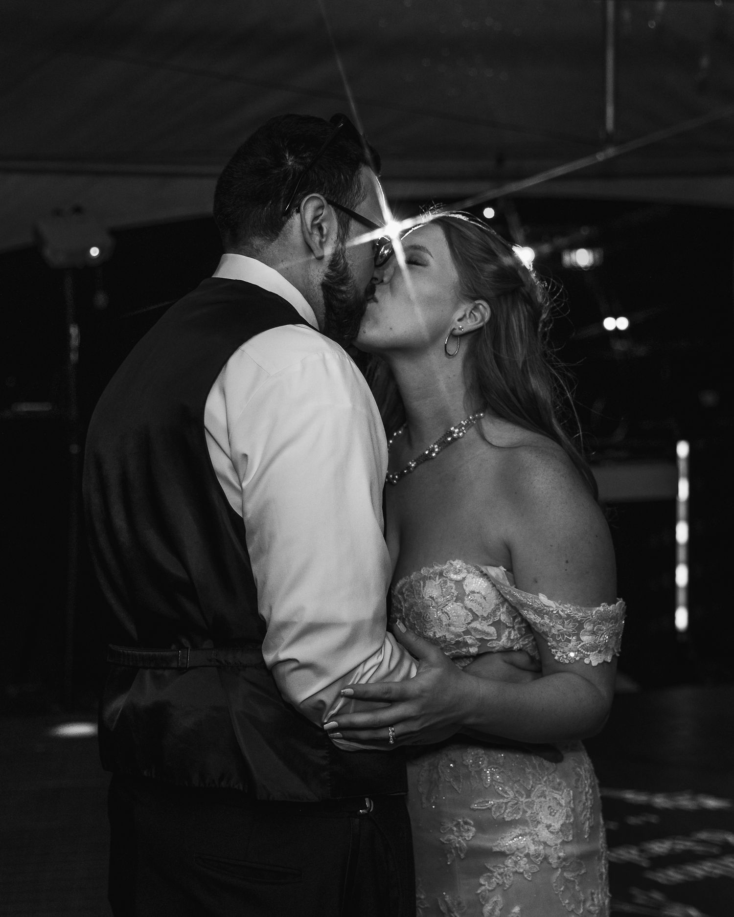 A black and white photo of a couple sharing an intimate kiss during their wedding dance.