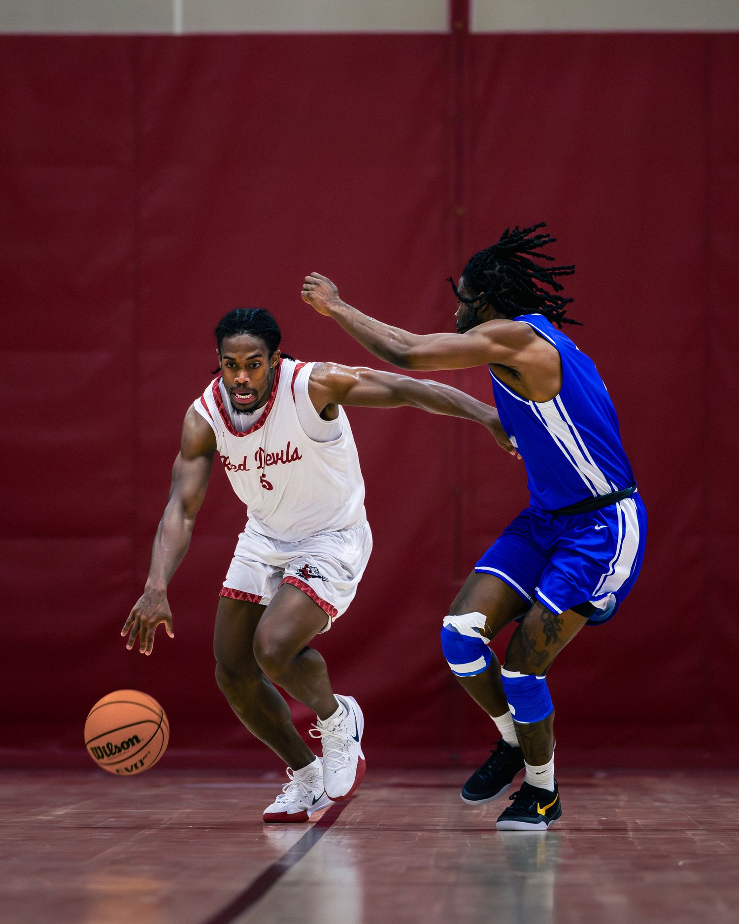 Basketball players in red and blue uniforms battle for possession during an intense defensive play on the court.