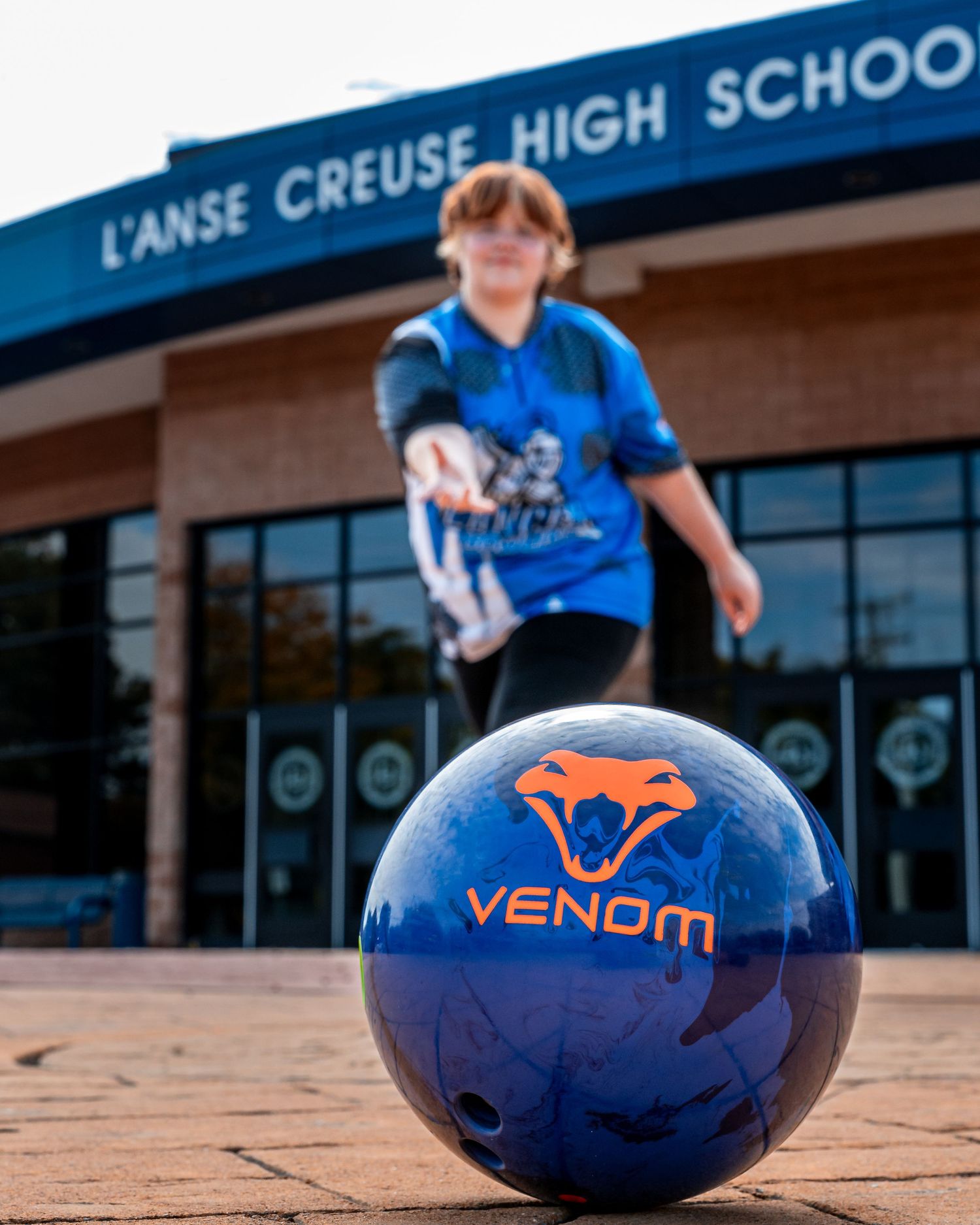 Navy blue football with orange fox logo rests on brick pavement outside school building.