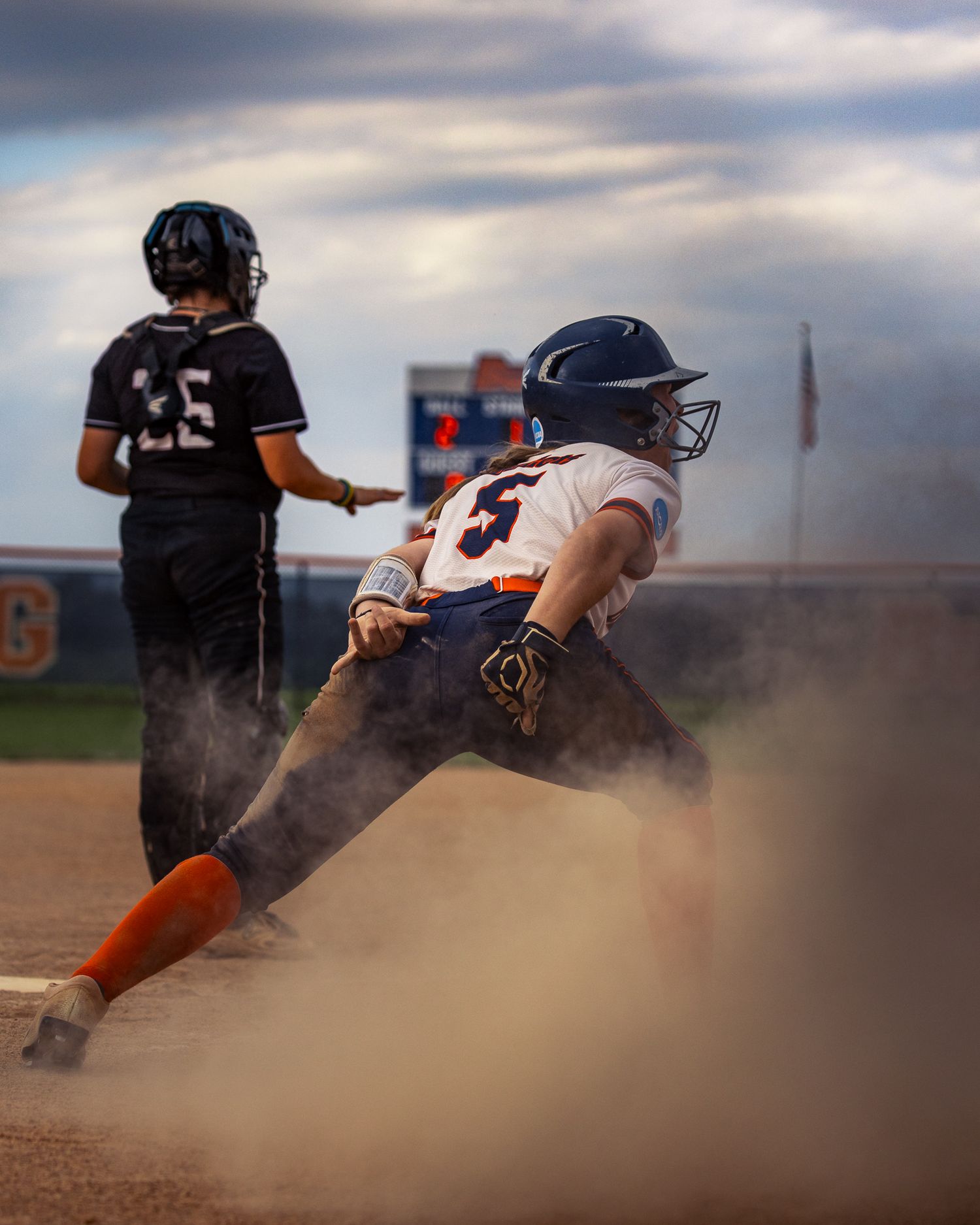 Baseball player slides into base creating a cloud of dust during an intense game.