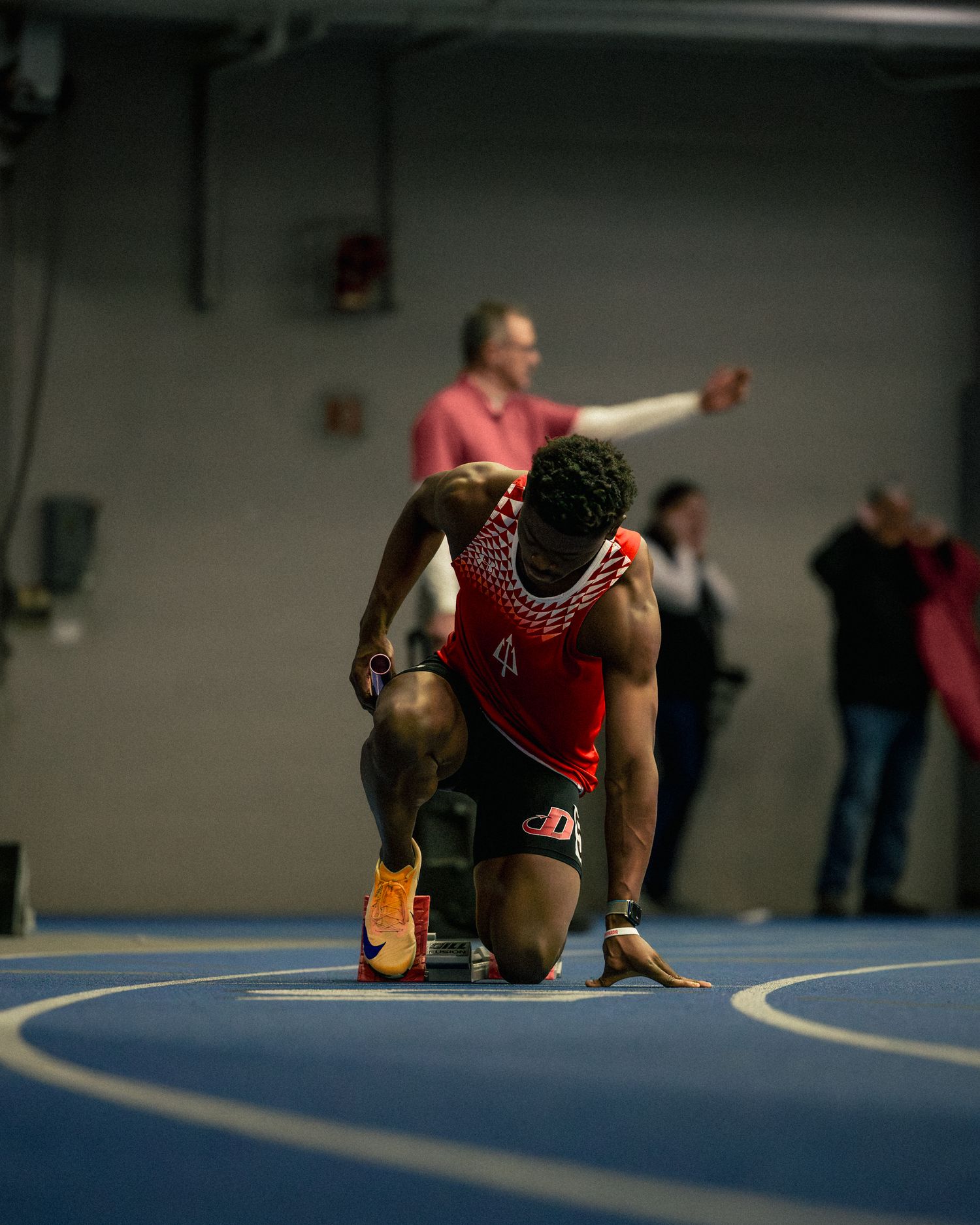 Multiple exposure sequence showing athlete's starting position on indoor running track.