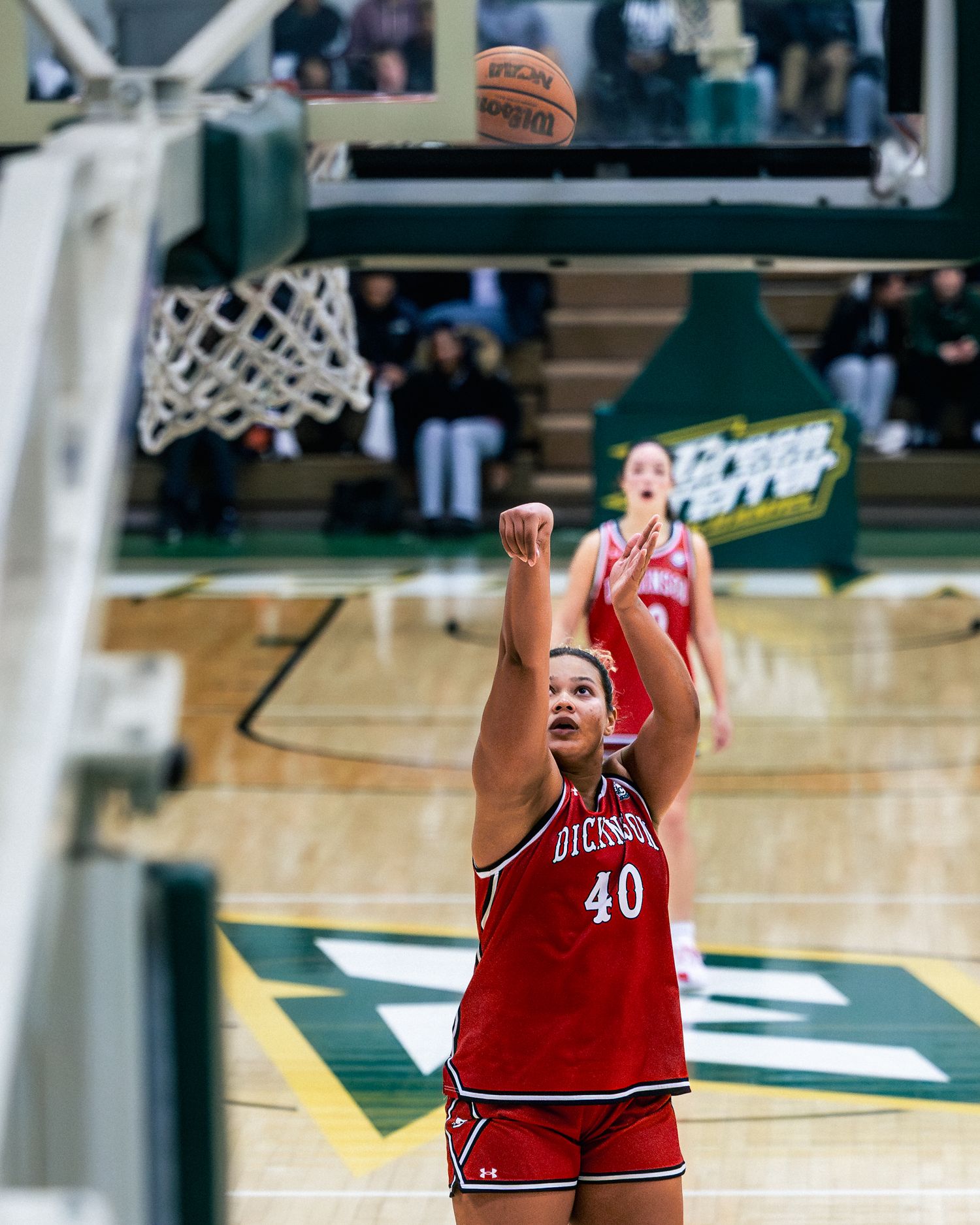 Basketball player in red jersey takes a shot at the basket during a competitive game.