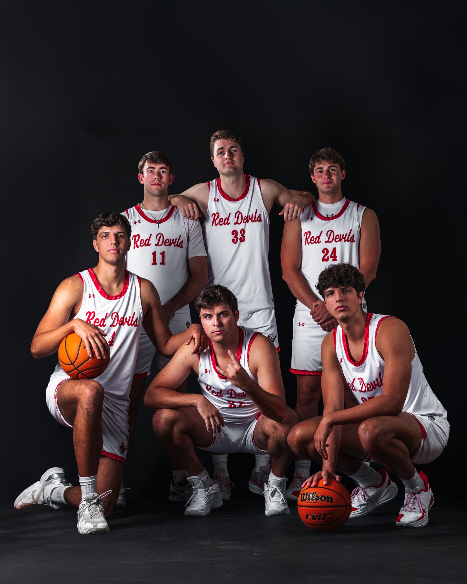 Basketball team members pose in white uniforms against a dark background in a series of studio portraits.