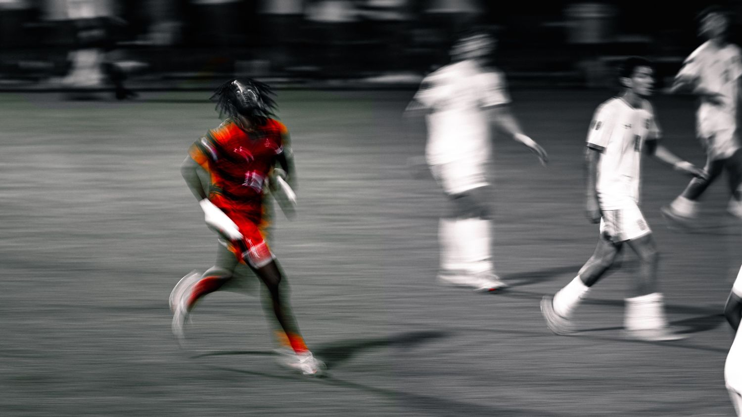 Motion blur photo of soccer player in red jersey running past opponents in white uniforms during match.