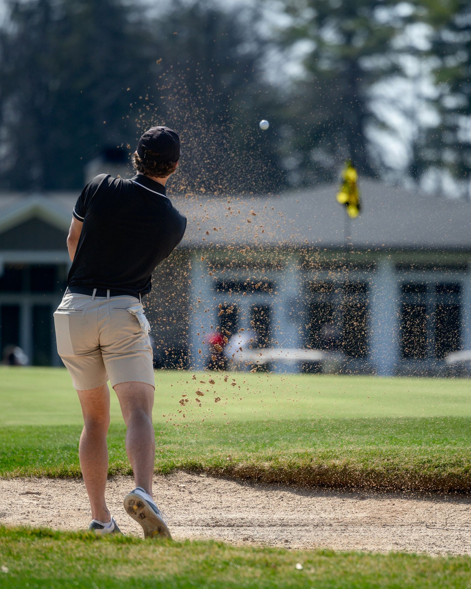 A golfer hits from a sand bunker creating a dramatic spray of sand during their golf shot at a course.