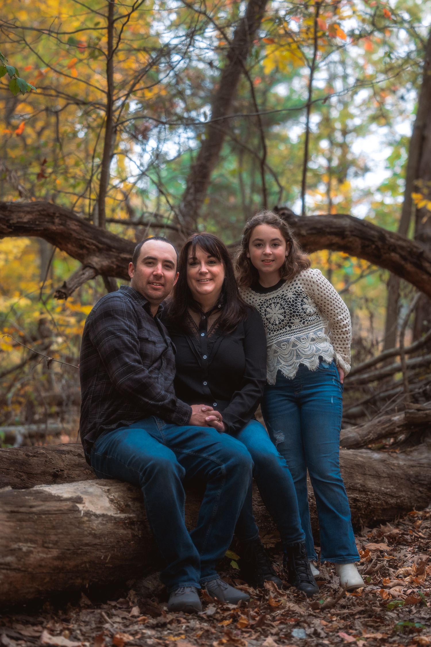A group sits together on a fallen log surrounded by autumn foliage and golden leaves in a forest setting.
