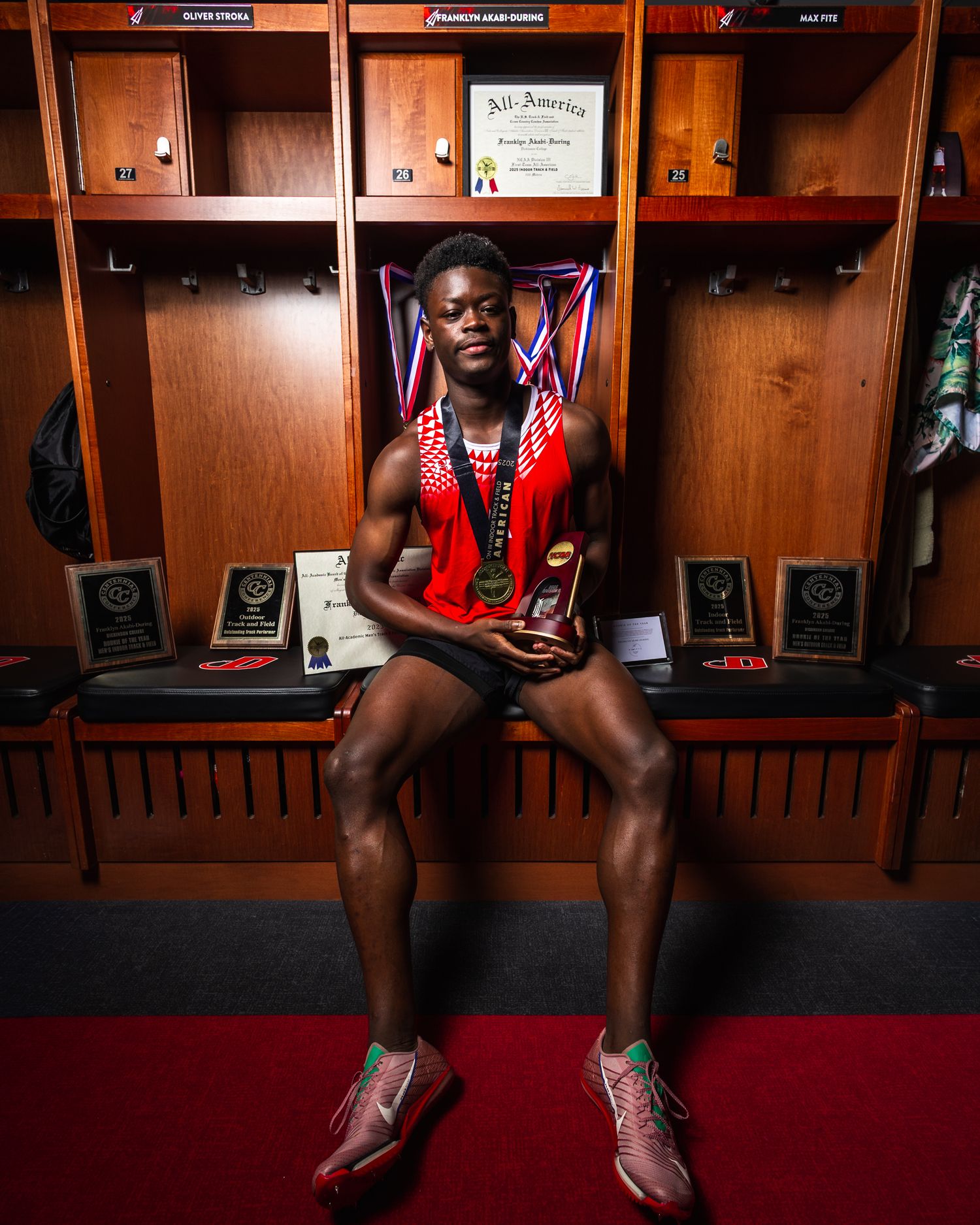 Professional athlete sits in a wooden locker room wearing a red jersey and white shoes.