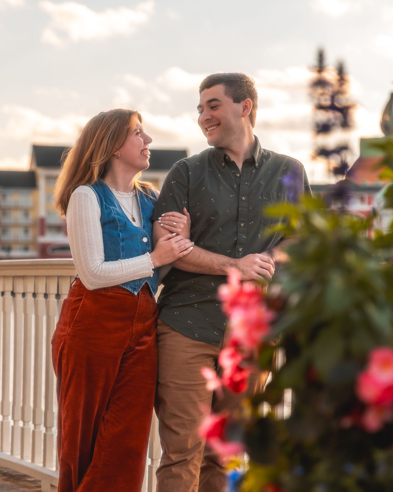 A couple shares a romantic moment dancing together on a porch at sunset with pink flowers in the foreground.