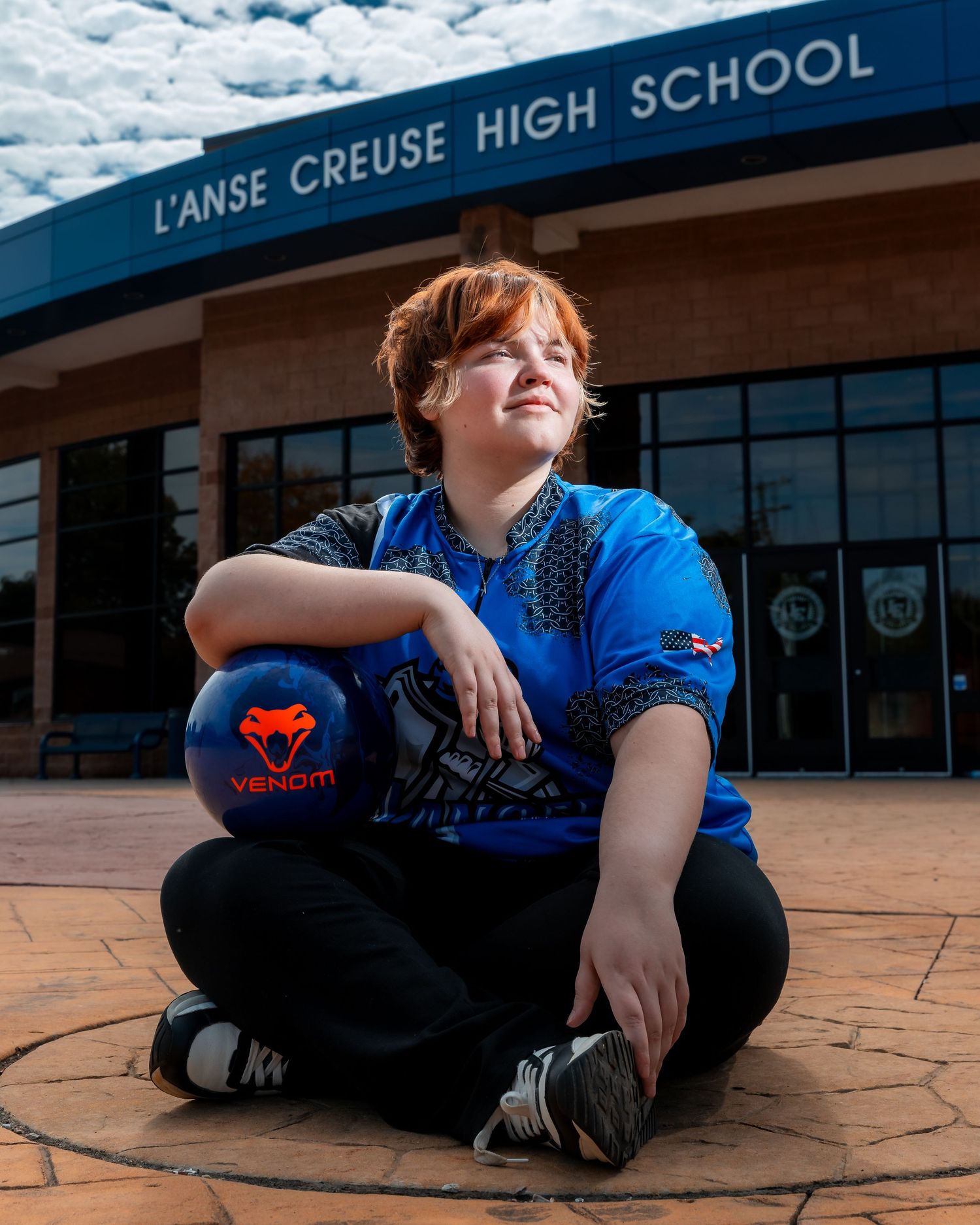 Student sits on gymnasium floor with L'Anse Creuse High School signage visible in background.