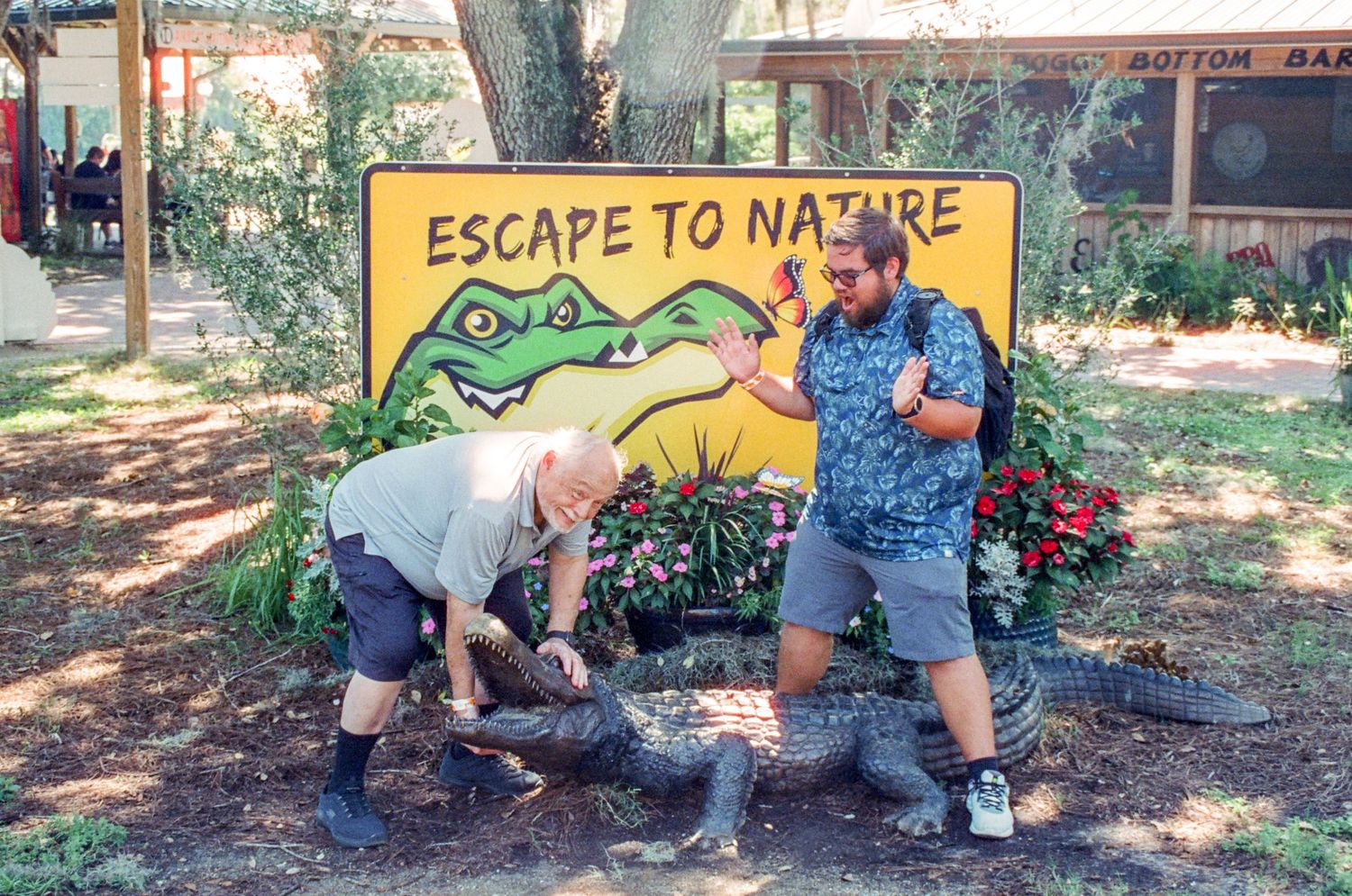 Two people pose playfully by a colorful Nature Escape alligator mural.