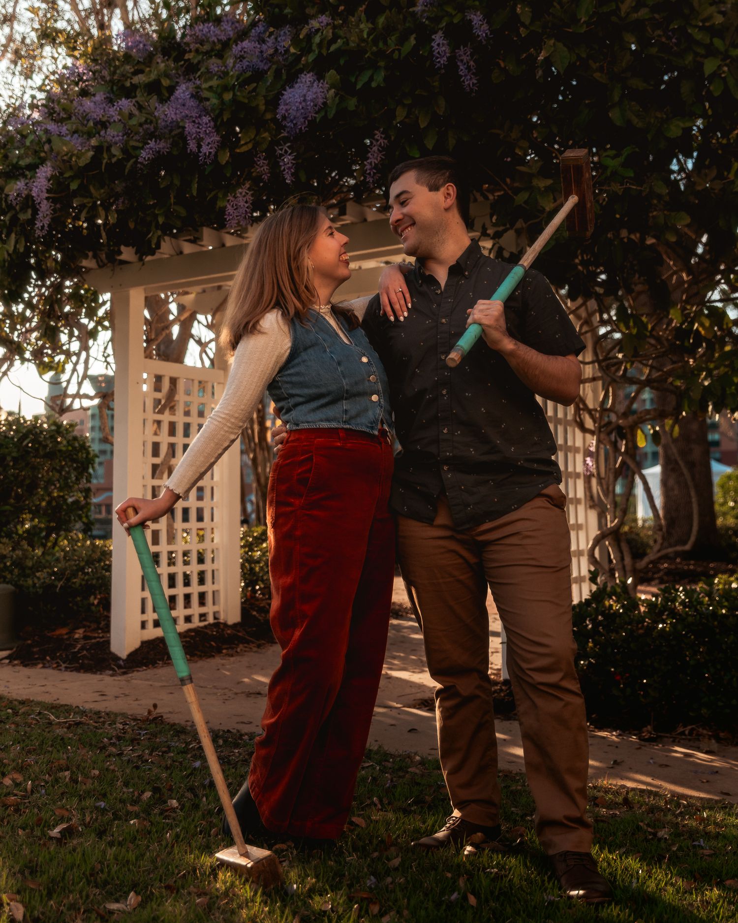 A couple dances together in a garden setting at sunset with flowering trees in the background.