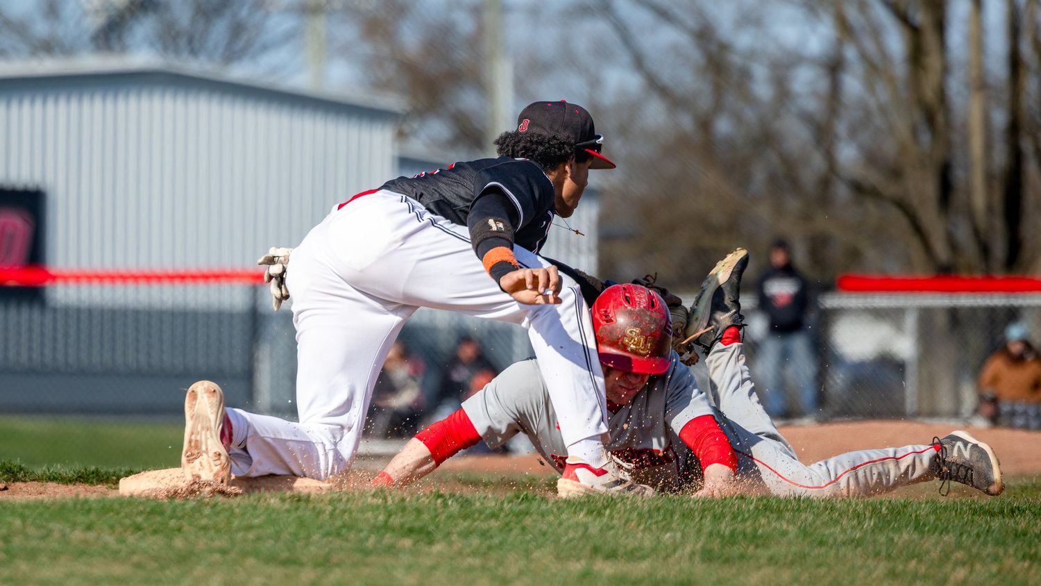 Baseball player in white uniform slides into base during competitive game action on sunny day.