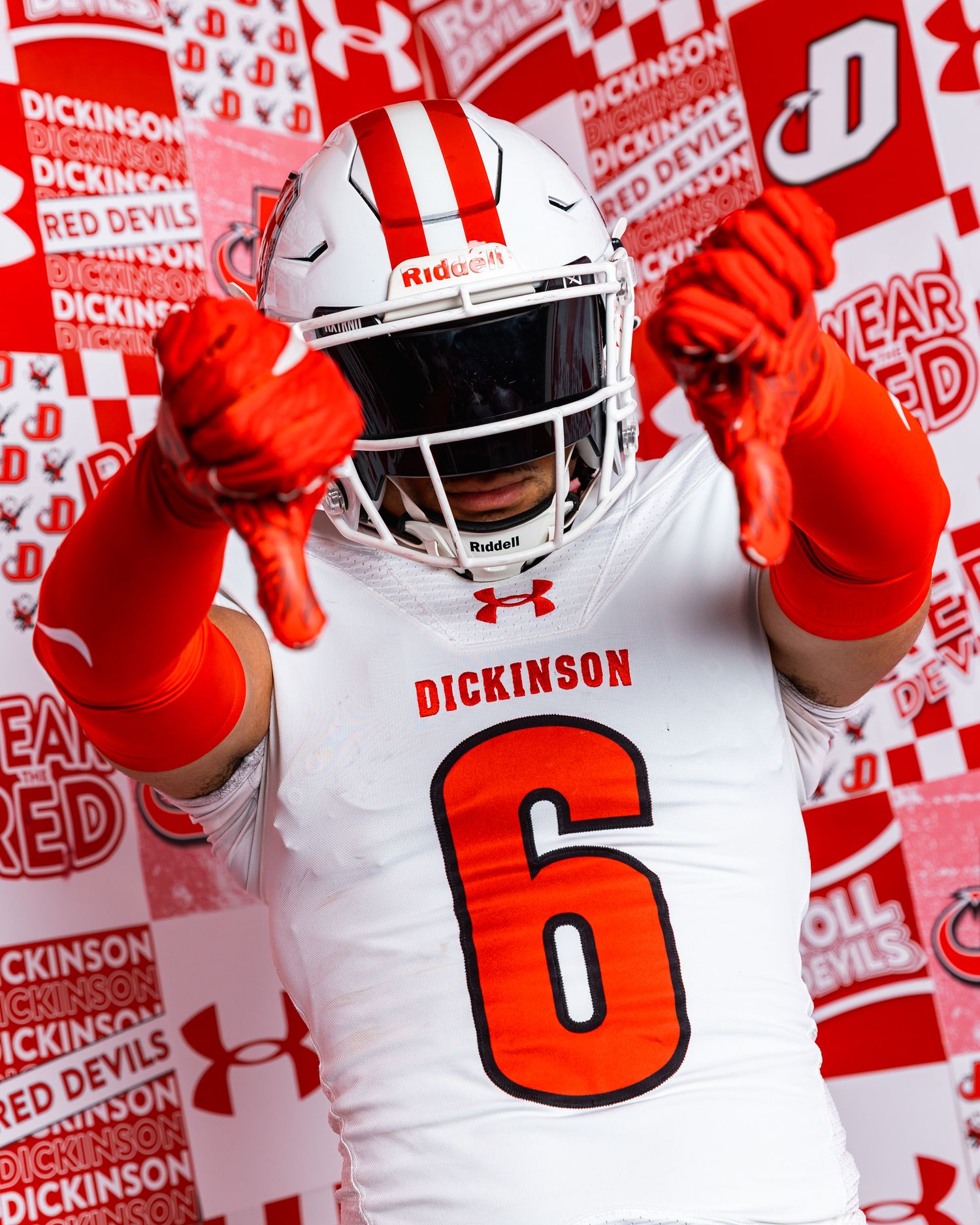 Dickinson Red Devils football player #6 in white uniform with orange gloves posing in front of branded backdrop.