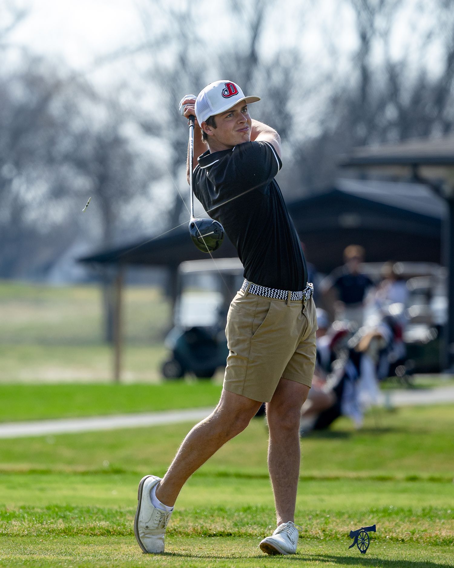 A golfer follows through on their swing during a round of golf on a grassy course.