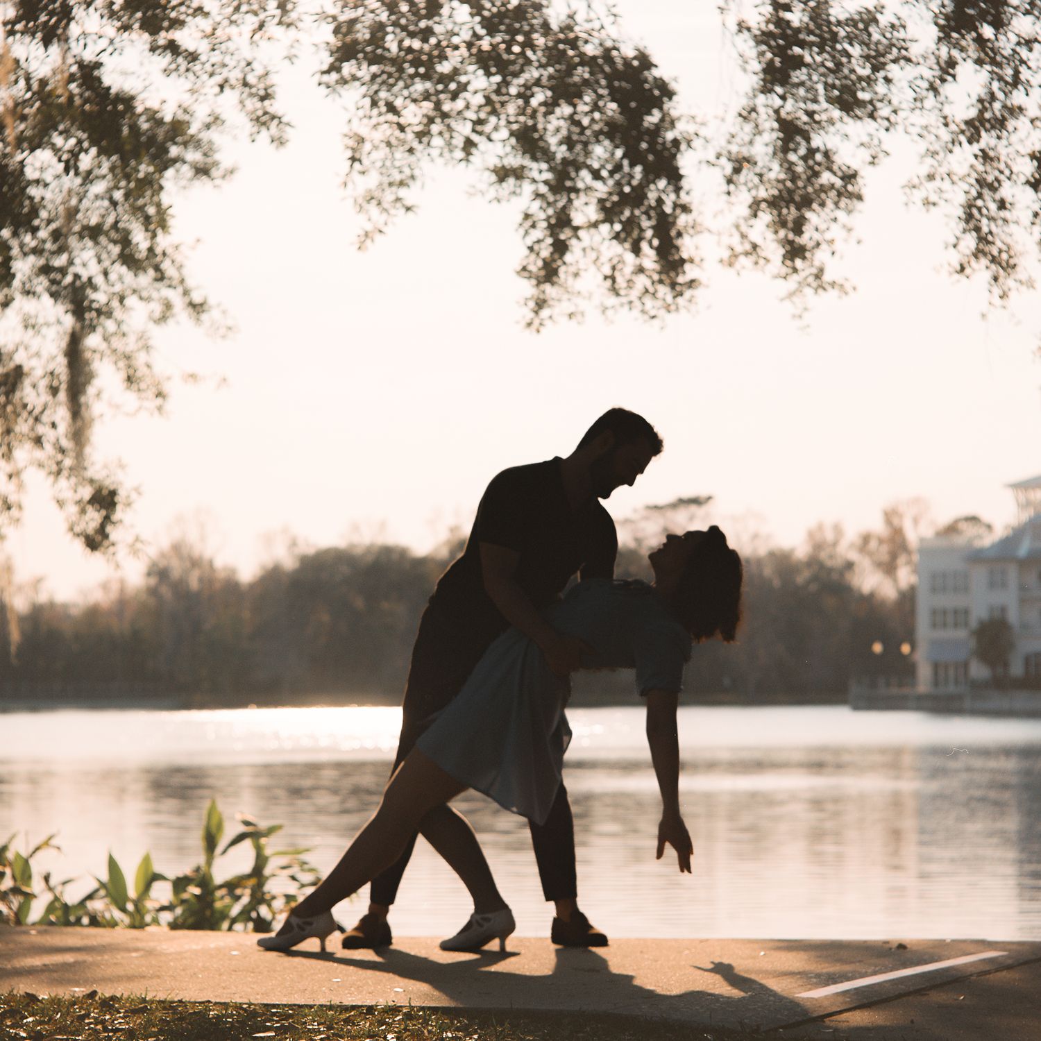 Silhouetted person practicing yoga poses at sunset by a tranquil lake with trees in the background.