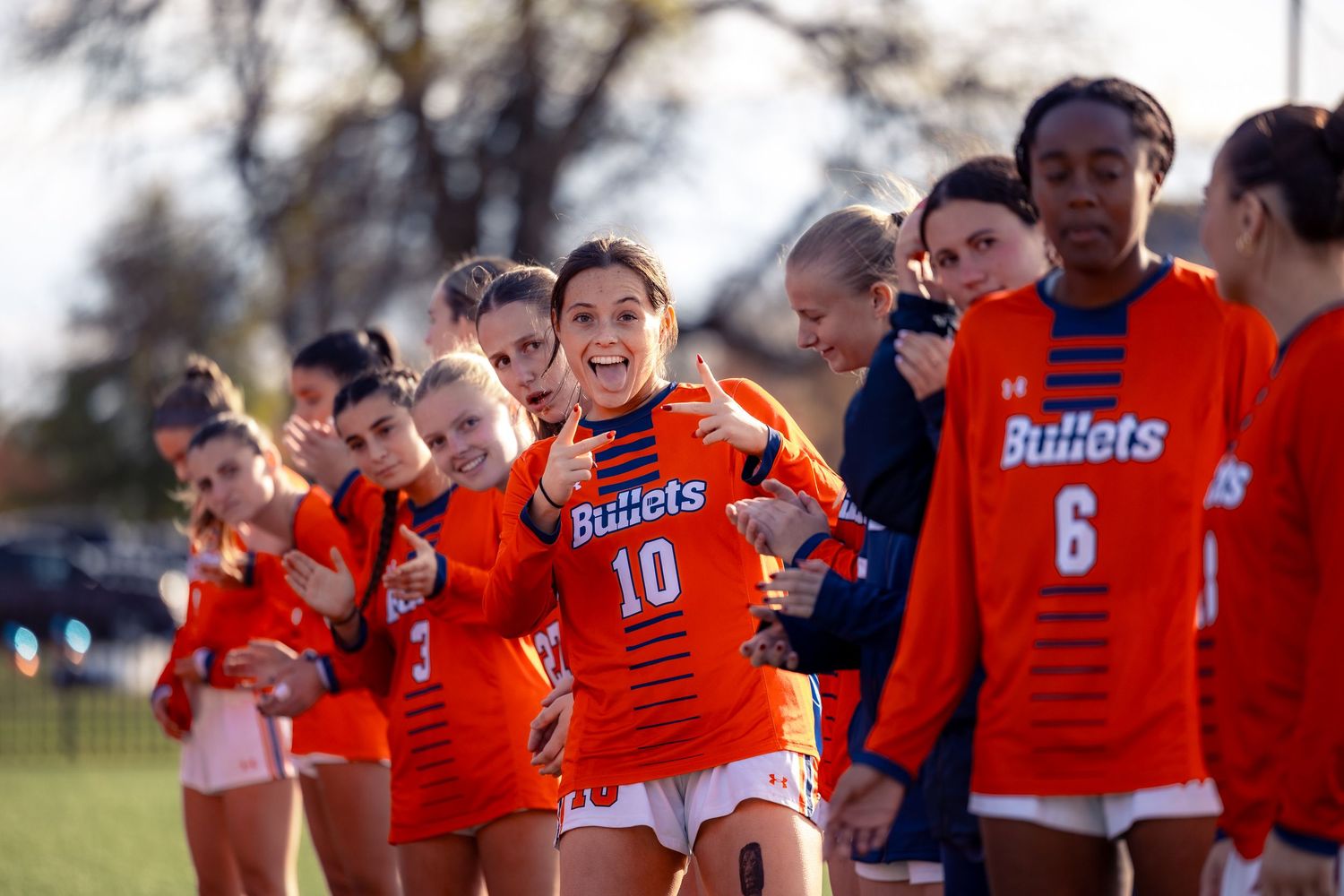 High school sports team members in orange uniforms stand together on a field during practice or game day.