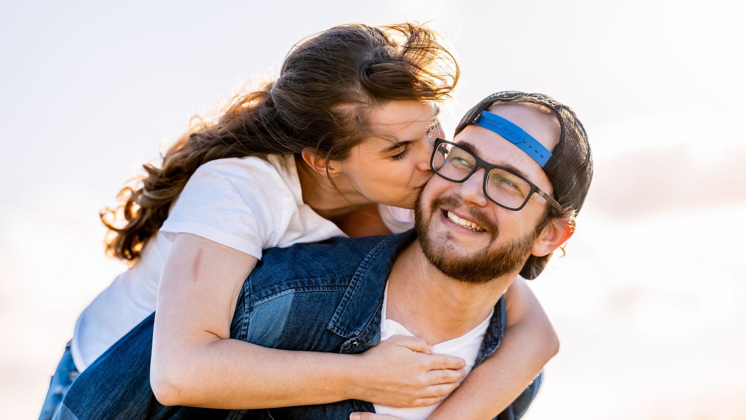 A couple embraces and smiles together in a series of romantic poses against a bright background.