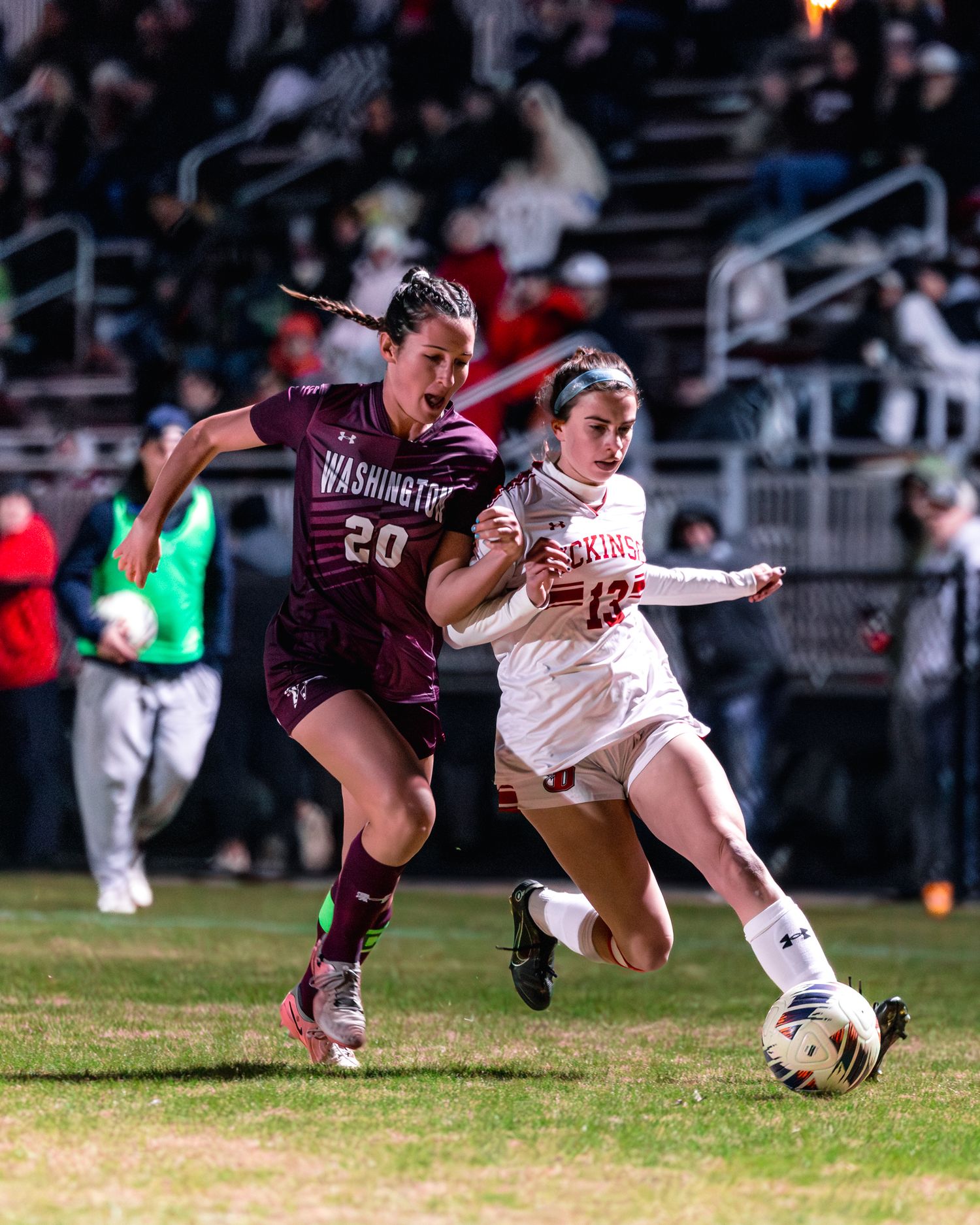 Two soccer players battle for possession of the ball during an intense match between maroon and white teams.
