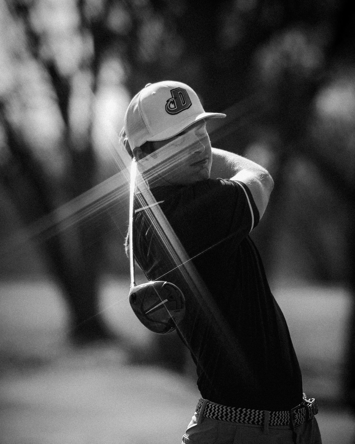 A black and white photo of a golfer mid-swing on the course, showing the follow-through motion.