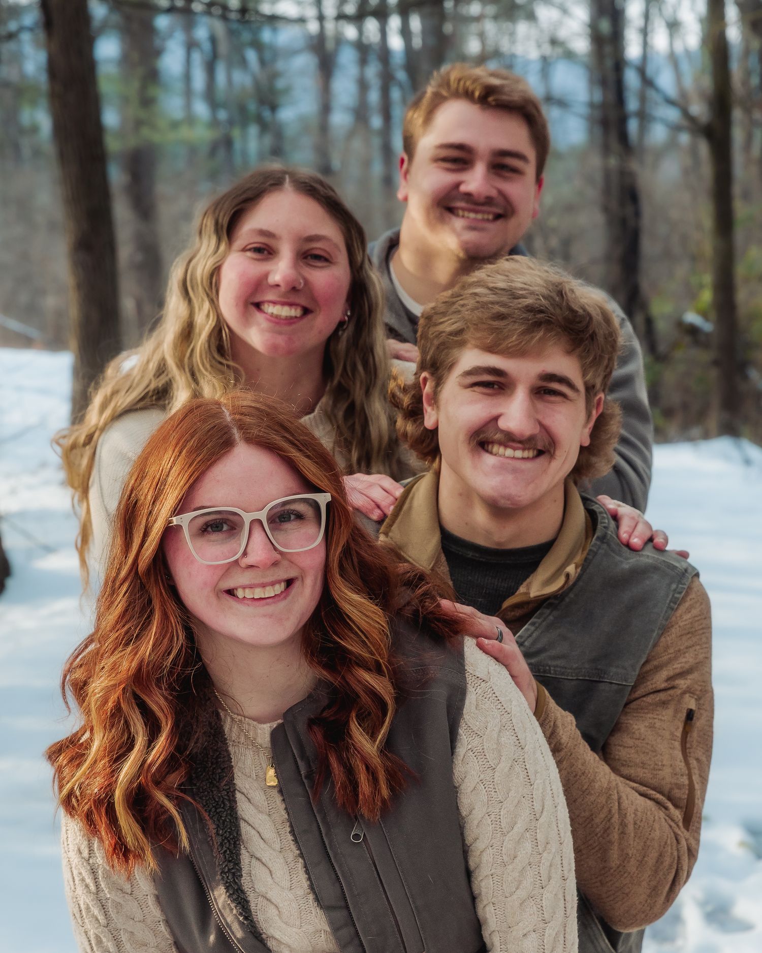 A series of five winter portraits showing a couple posing together in a snowy forest setting.