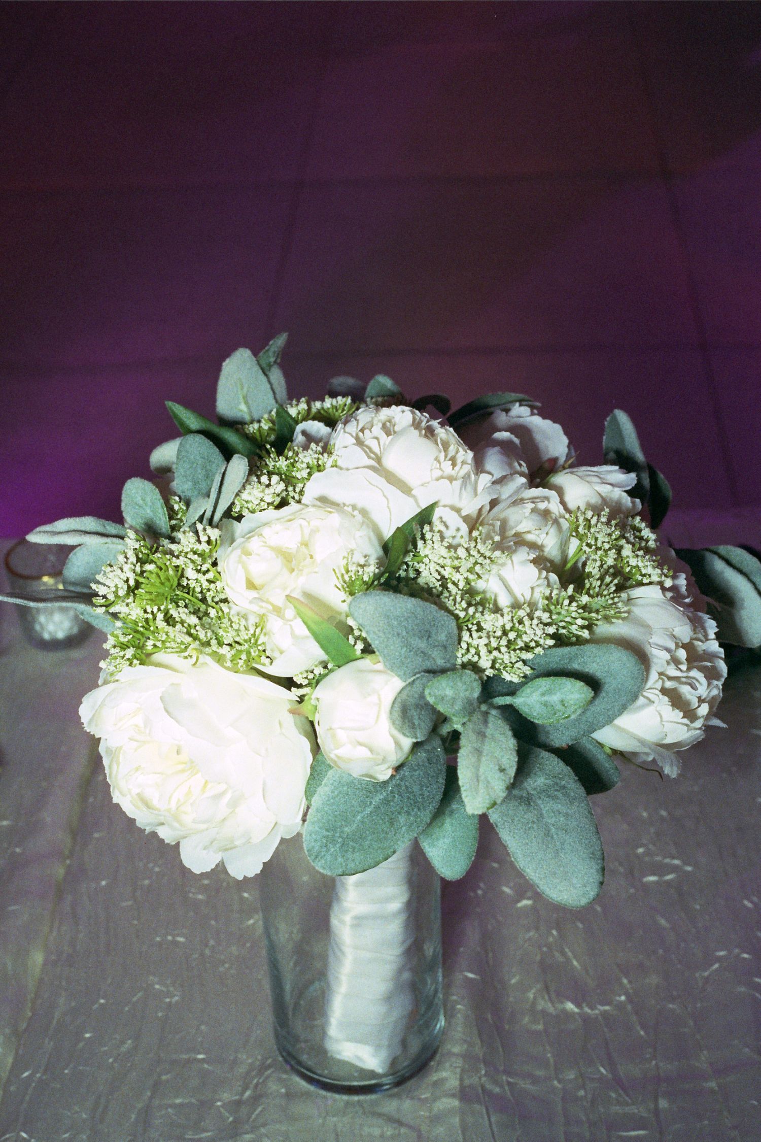 A row of elegant white floral arrangements with eucalyptus leaves in glass vases displayed against a dark background.