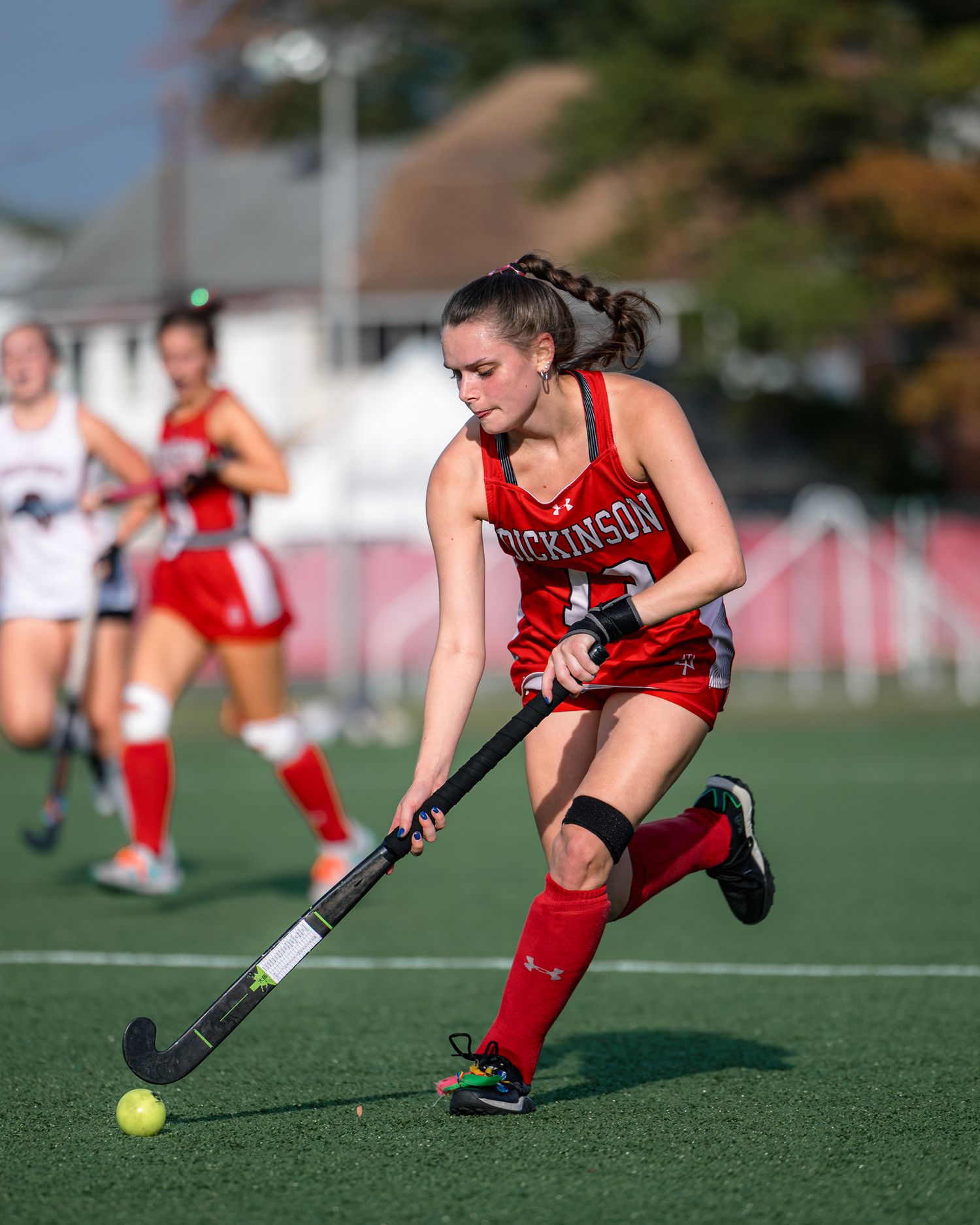 Field hockey player in red uniform lunges forward to control ball on artificial turf during competitive match.