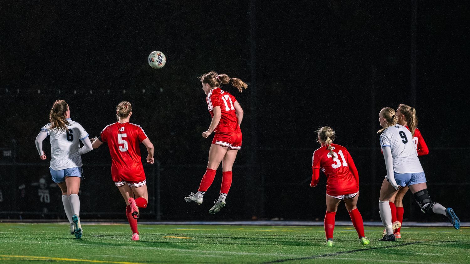 Soccer players compete for control of the ball during a nighttime match under bright stadium lights.