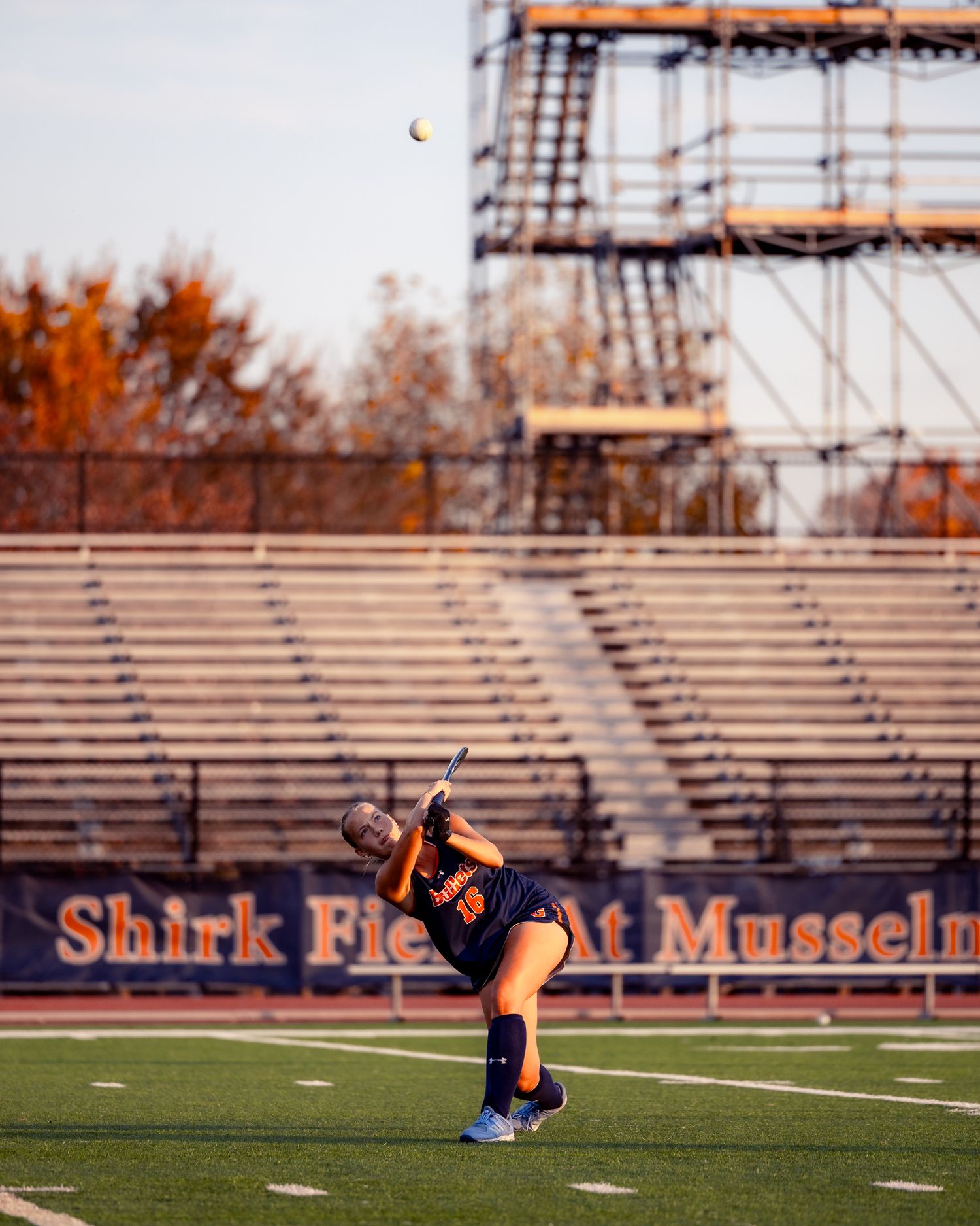 Soccer player in dark uniform practices kicking drills on an empty stadium field during golden hour lighting.