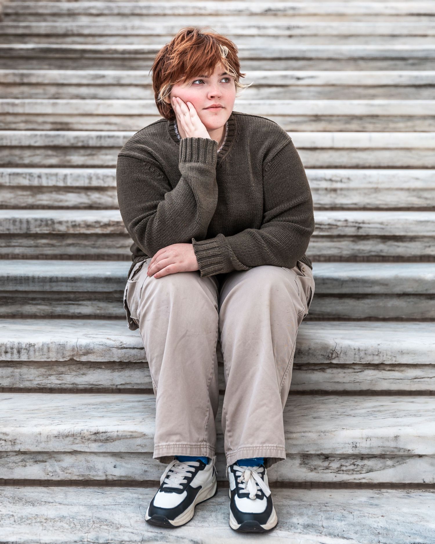 Person sitting on weathered wooden steps wearing brown sweater and khaki pants with black and white shoes.