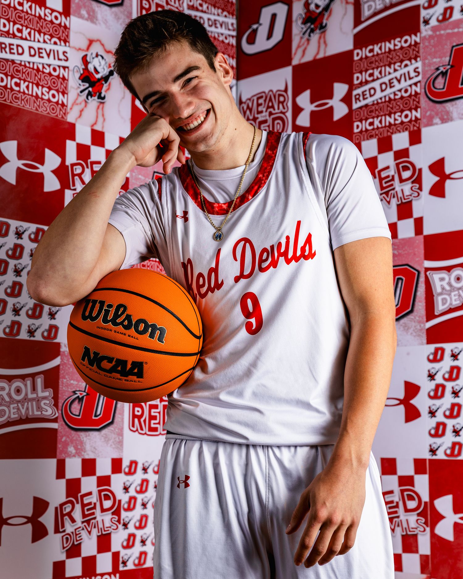 Basketball players smile and pose casually with basketballs against a red and white branded backdrop.