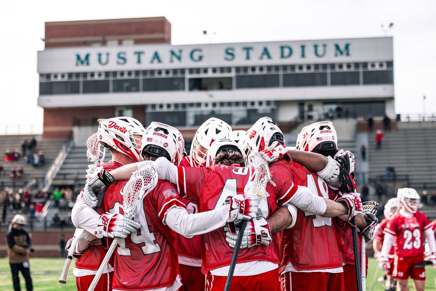 SMU football players in red and white uniforms huddle together on the field at Mustang Stadium during a game.