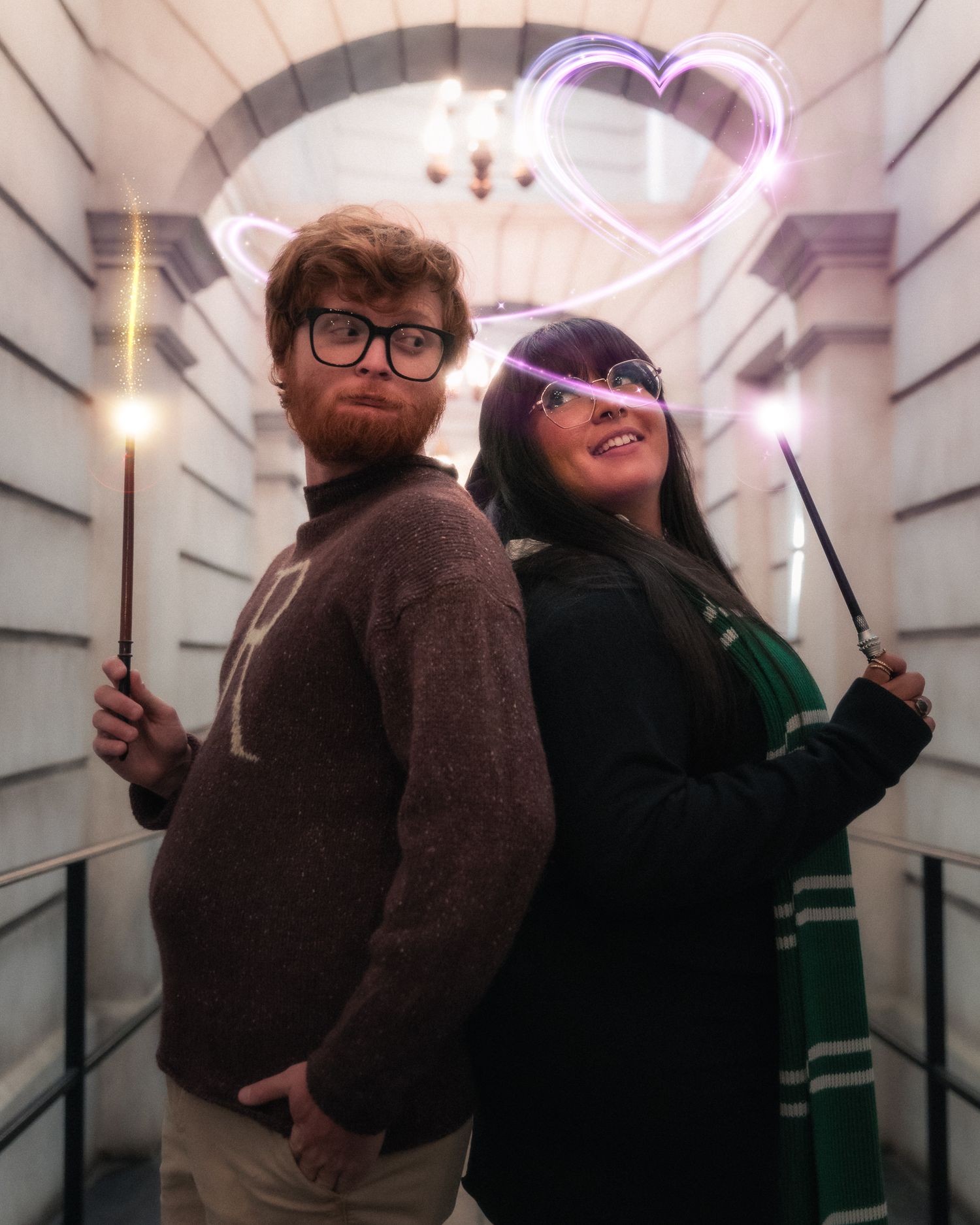 Two people pose playfully in a white hallway with neon pink lighting effects creating a dynamic atmosphere.