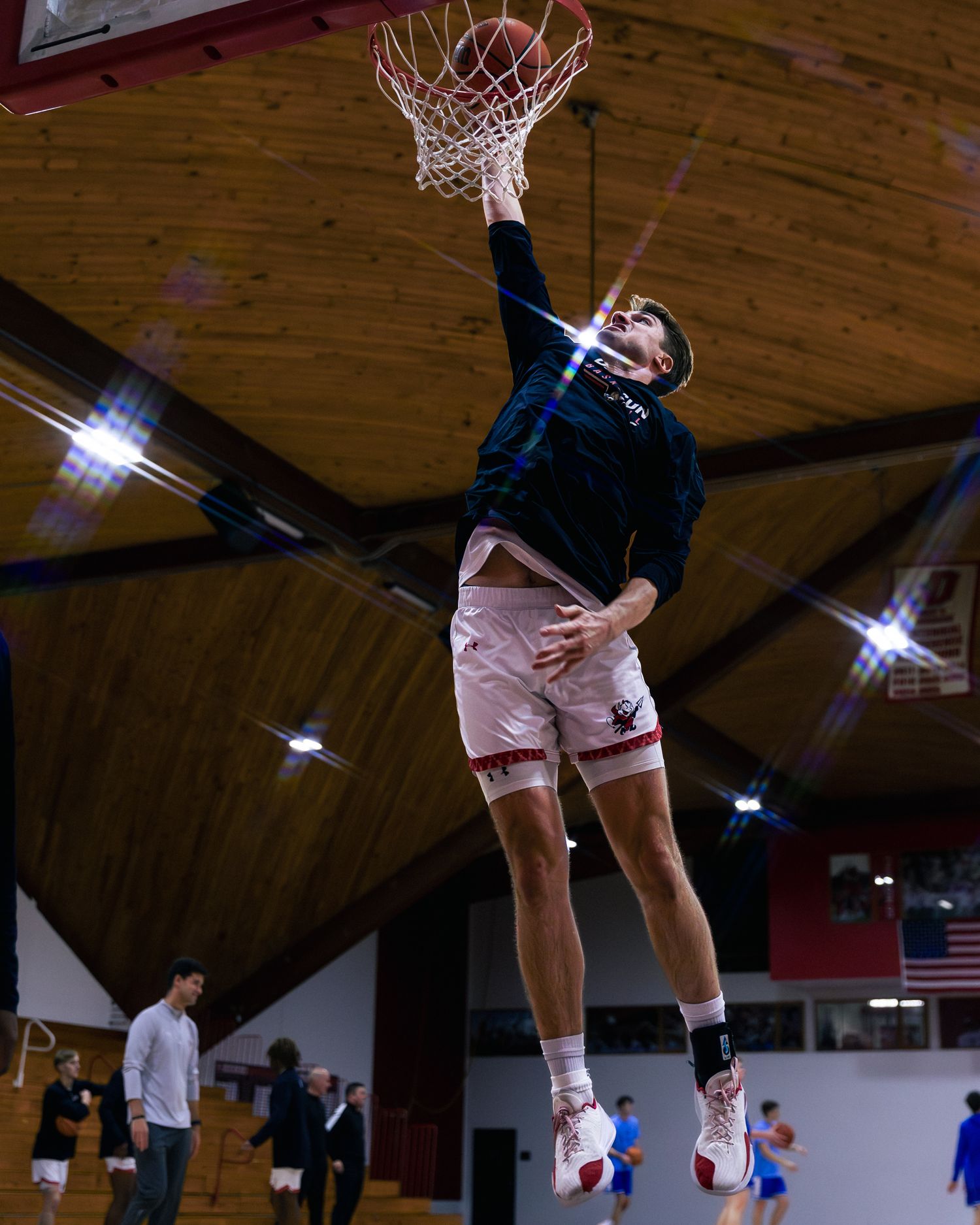 Basketball players leap high in a sequence of dynamic jump shots under indoor gym lighting.