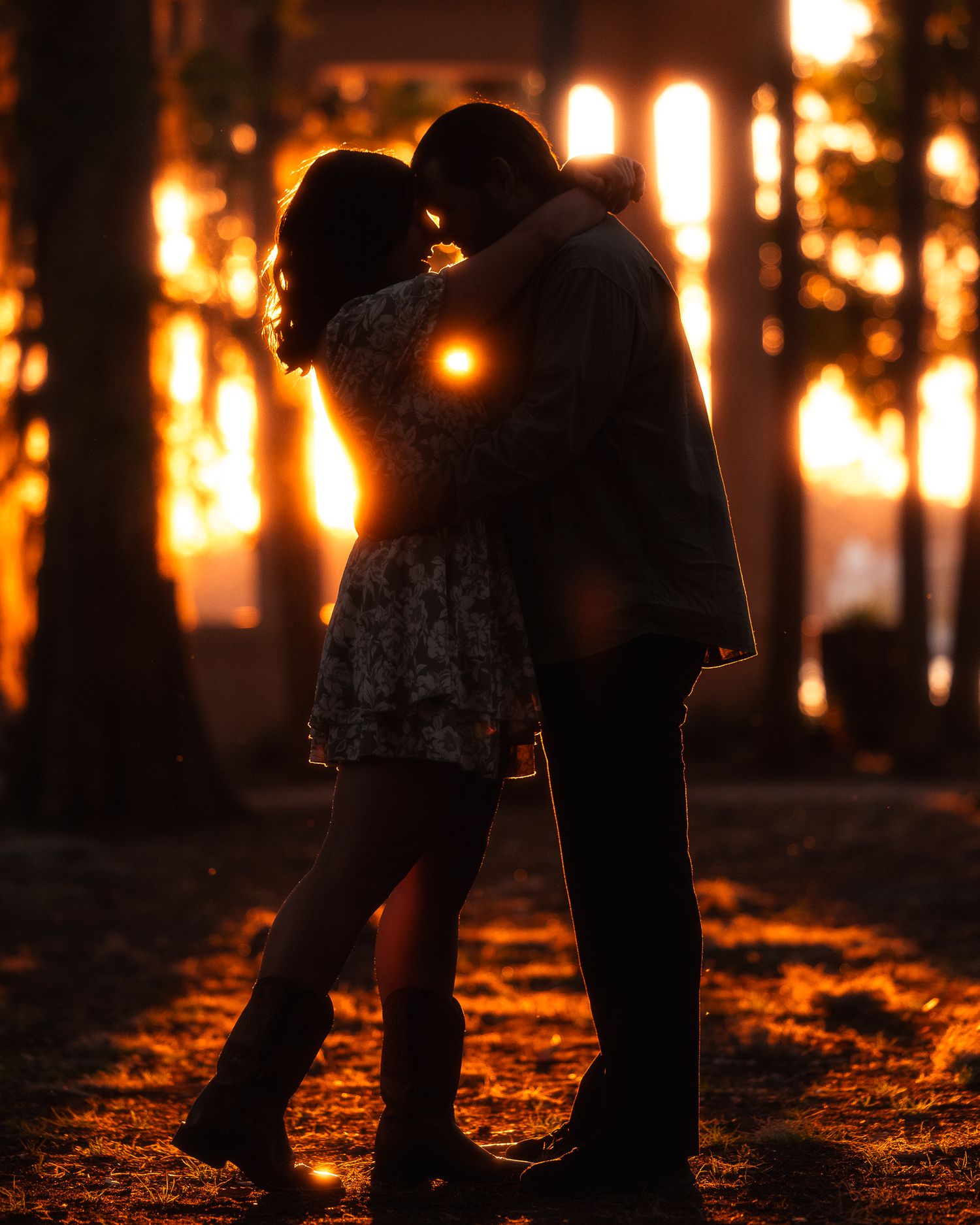 Silhouetted legs of people walking through a forest at sunset with glowing orange light filtering through trees.