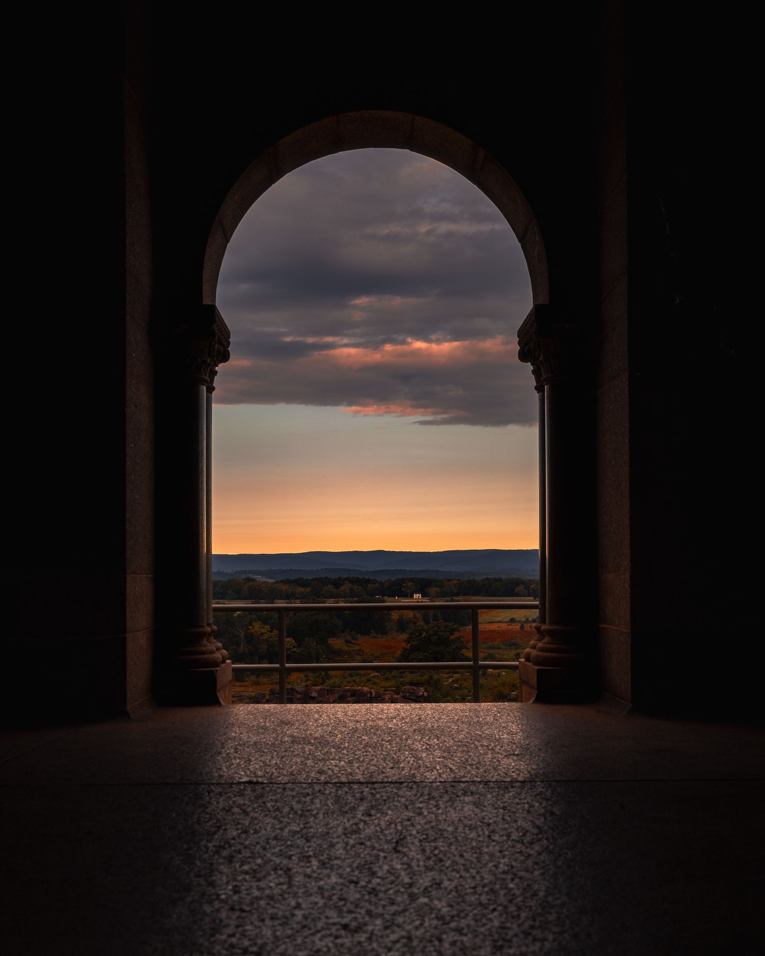 Dramatic sunset view through stone archways overlooking a mountainous landscape at dusk.