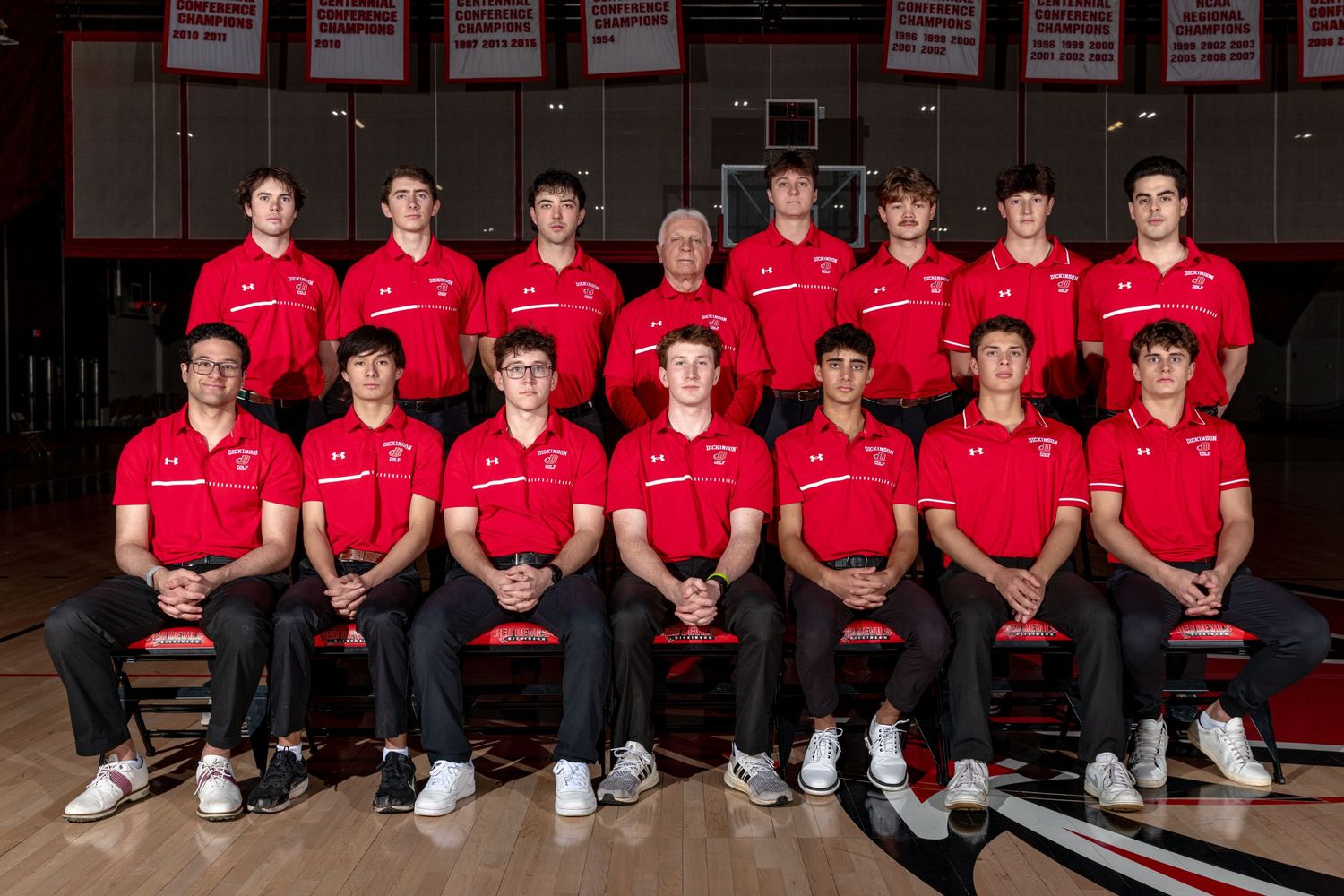 High school boys tennis team in red polo shirts poses for official group photo in gymnasium.
