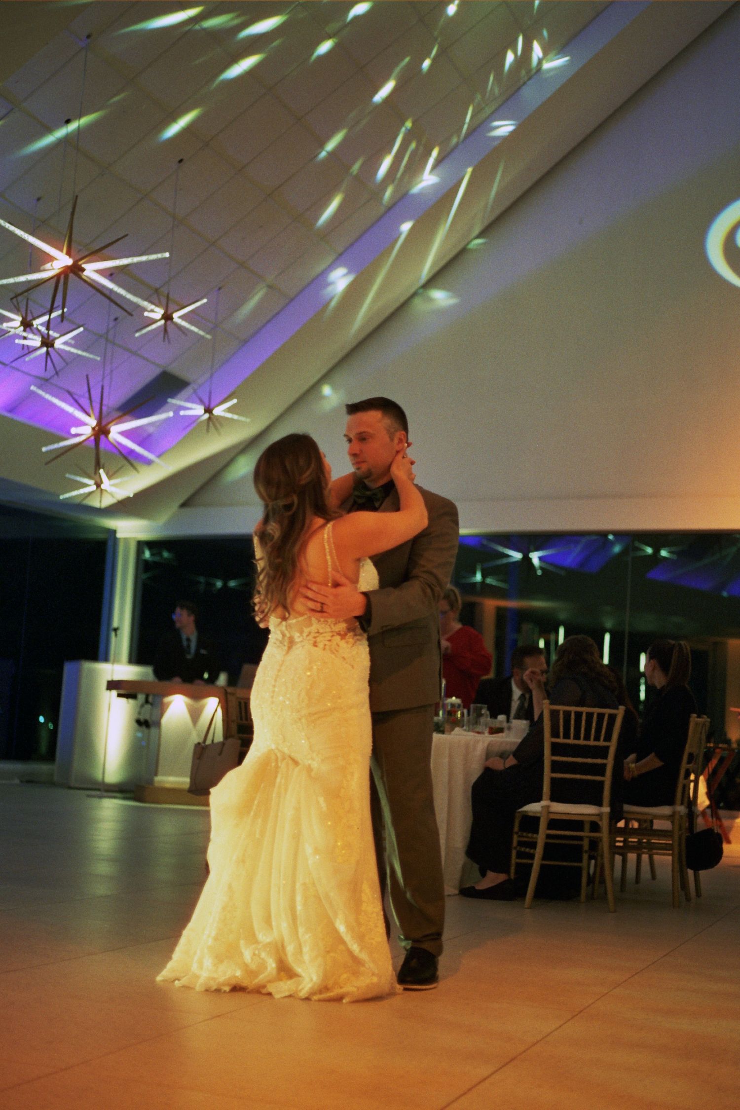 A couple shares a romantic dance moment on a wedding reception dance floor under colorful lighting.