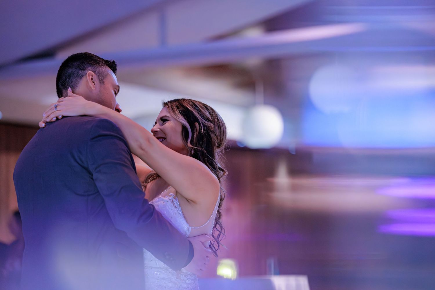 A couple shares a romantic dance together under purple and blue lighting at a wedding reception.