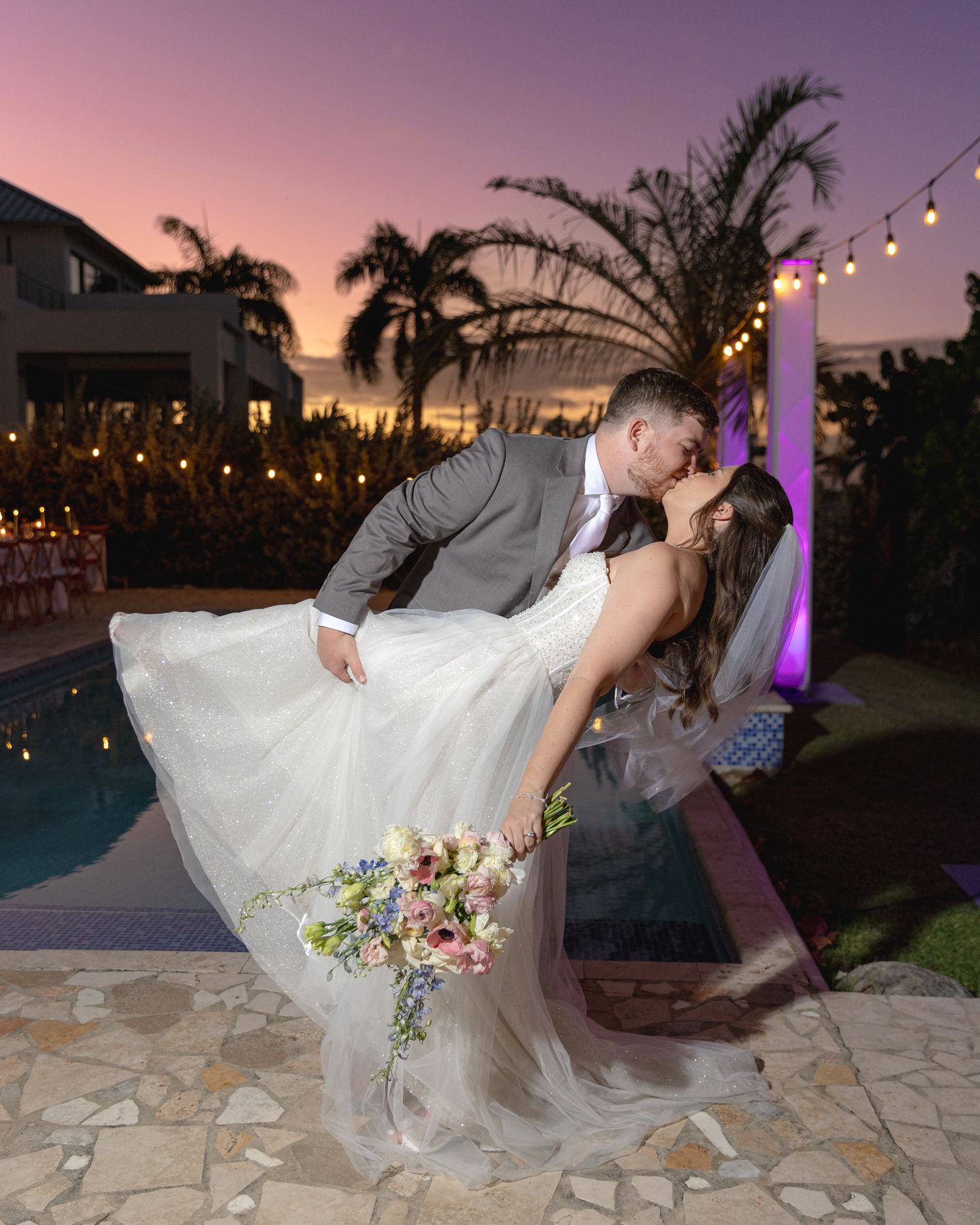 A romantic poolside dip pose at sunset with string lights and palm trees creating a tropical wedding ambiance. In Vieques Puerto Rico