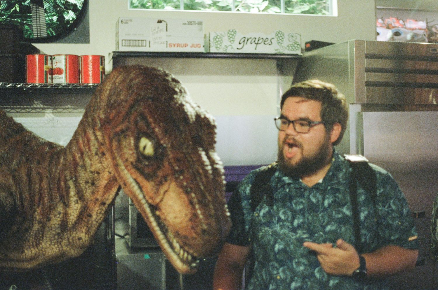 A person poses next to an animatronic velociraptor dinosaur display.