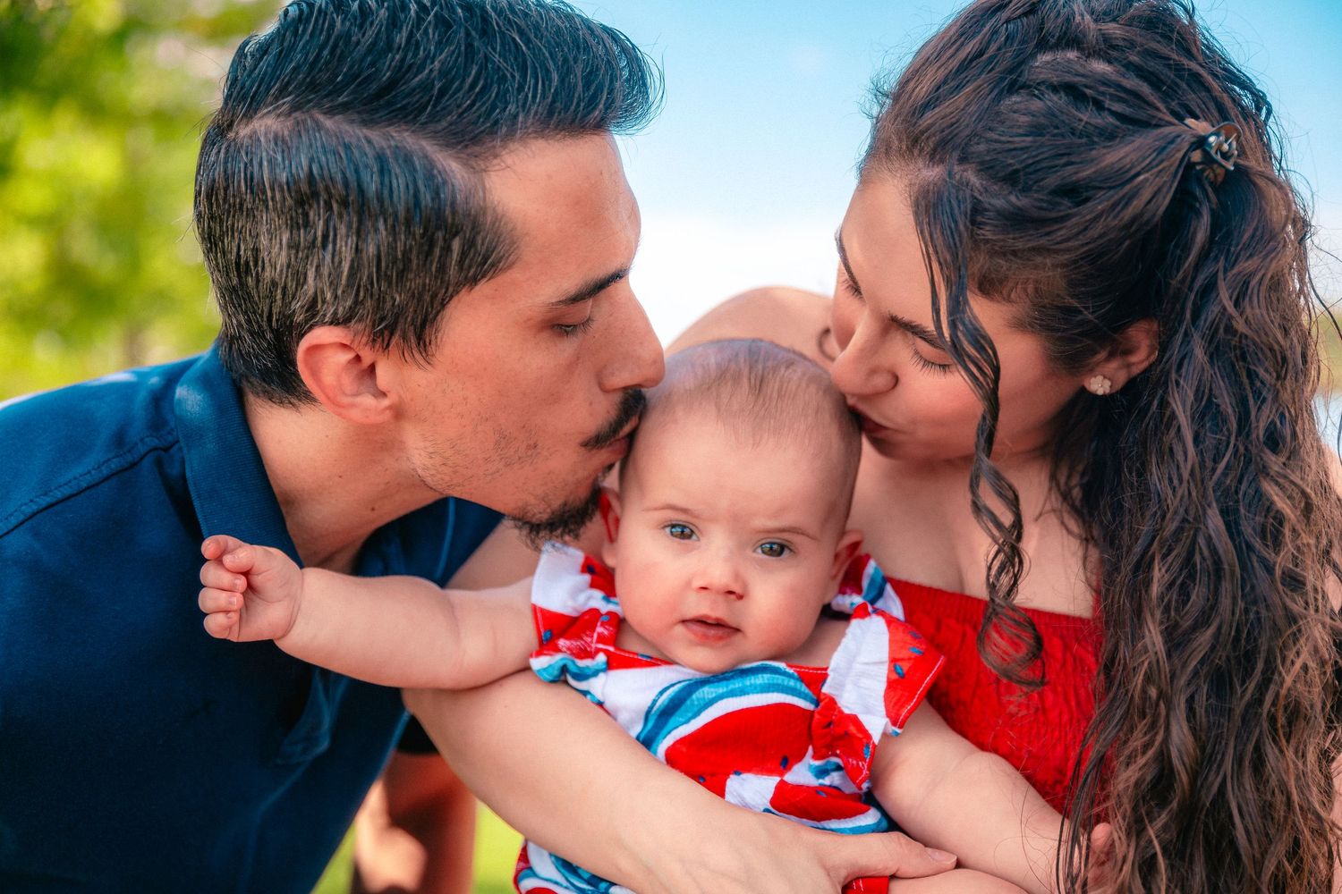 A loving family shares tender kisses and embraces in a series of outdoor photos with their baby in red clothing.