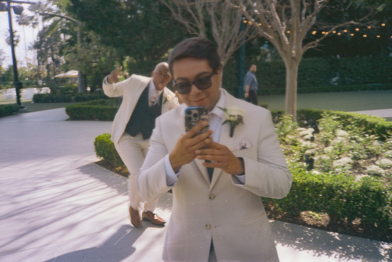 Person in white shirt and sunglasses enjoys a casual day outdoors in a sunny garden setting.