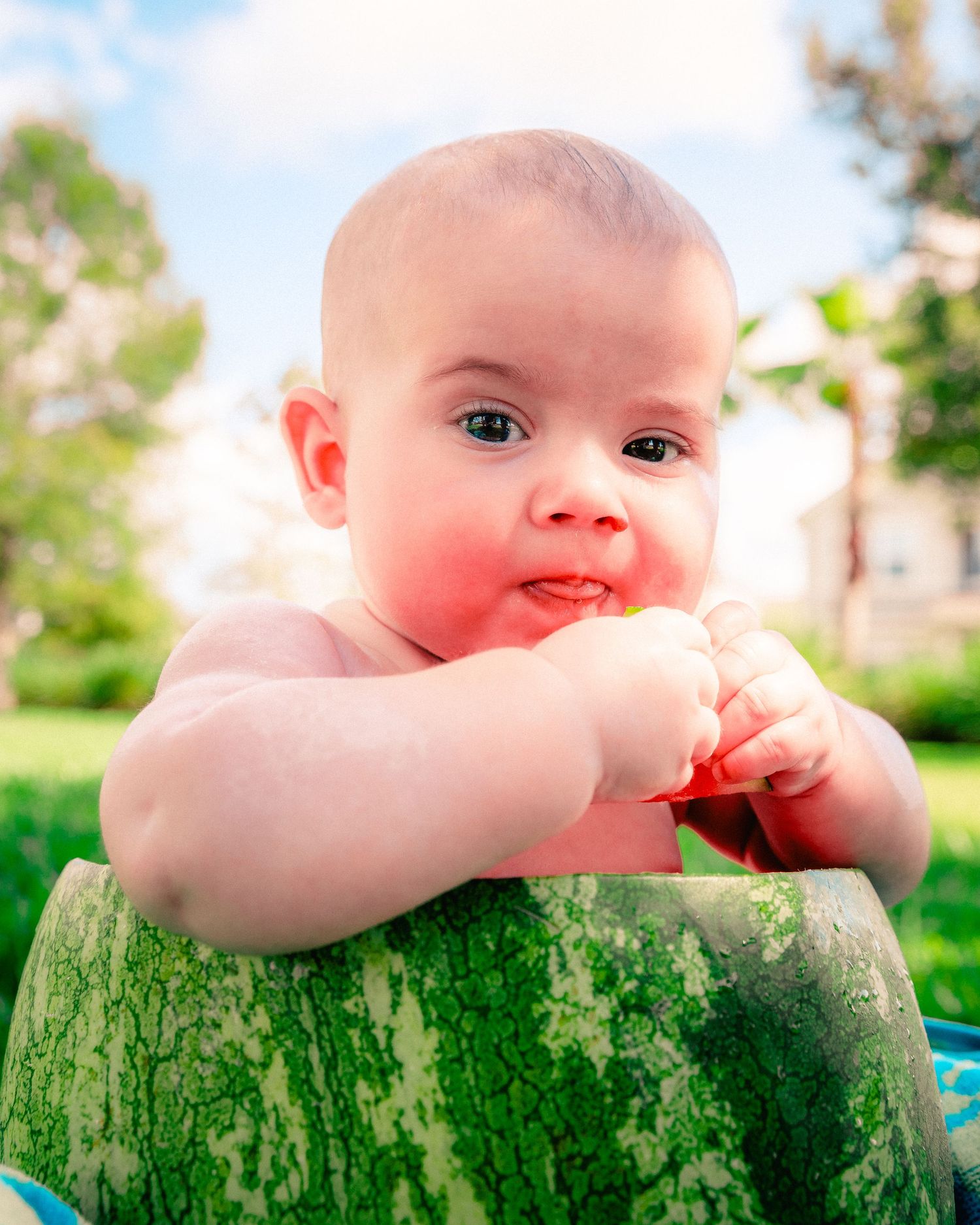 A baby rests their arms on a moss-covered tree stump while enjoying time outdoors on a sunny day.