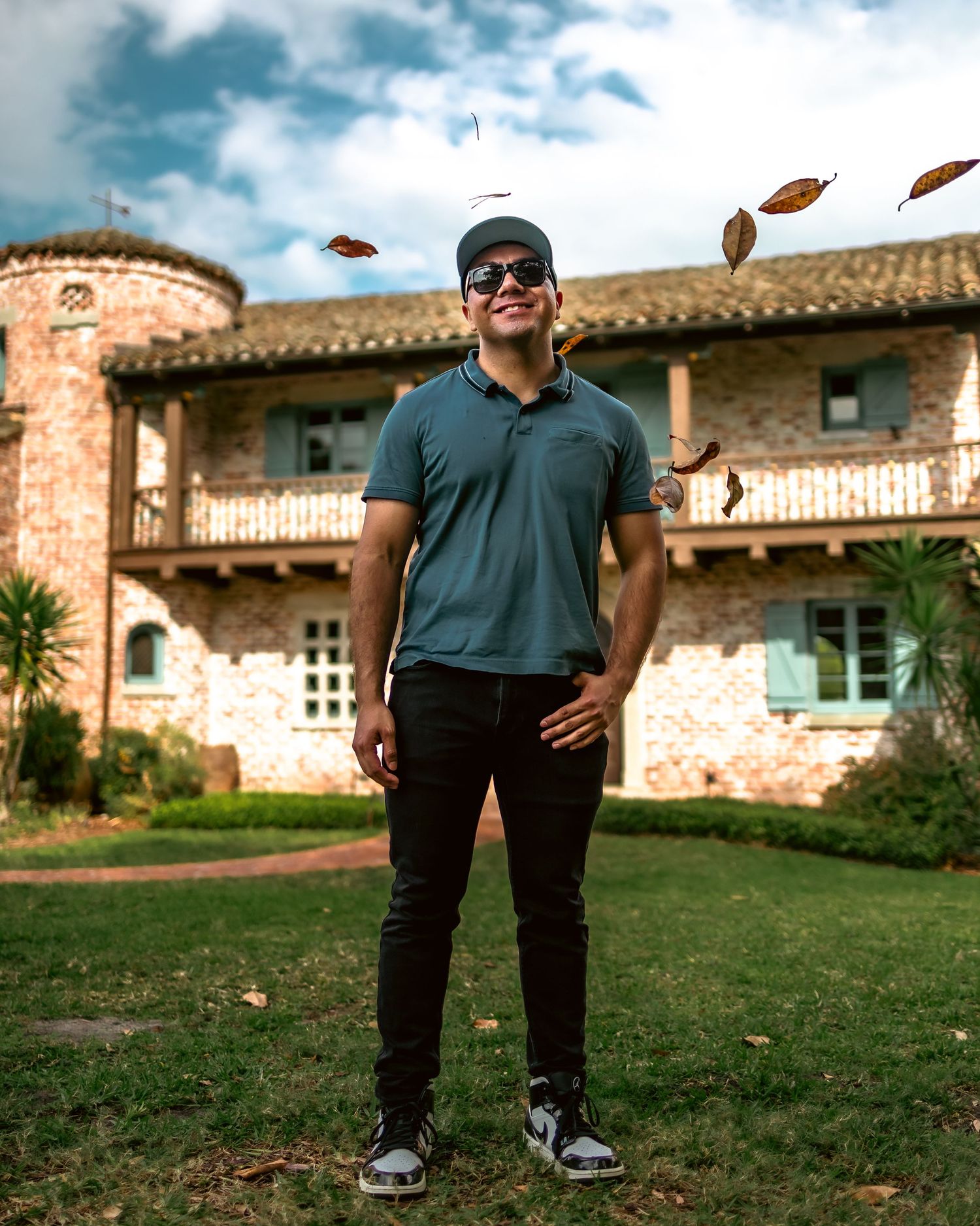Person standing in a rustic courtyard with autumn leaves falling against a cloudy sky backdrop.