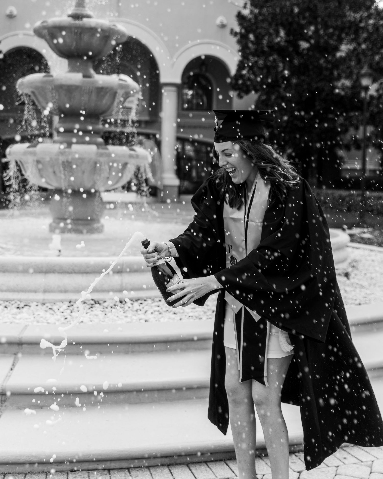 A black and white image shows people playing in falling snow near a fountain on a winter day.