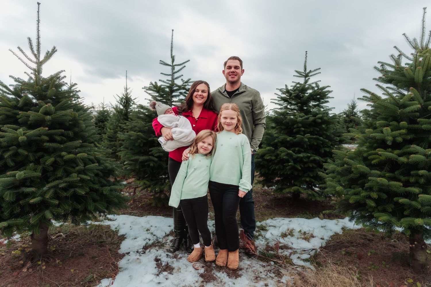 A group stands together at a Christmas tree farm on a cloudy winter day surrounded by evergreen trees.