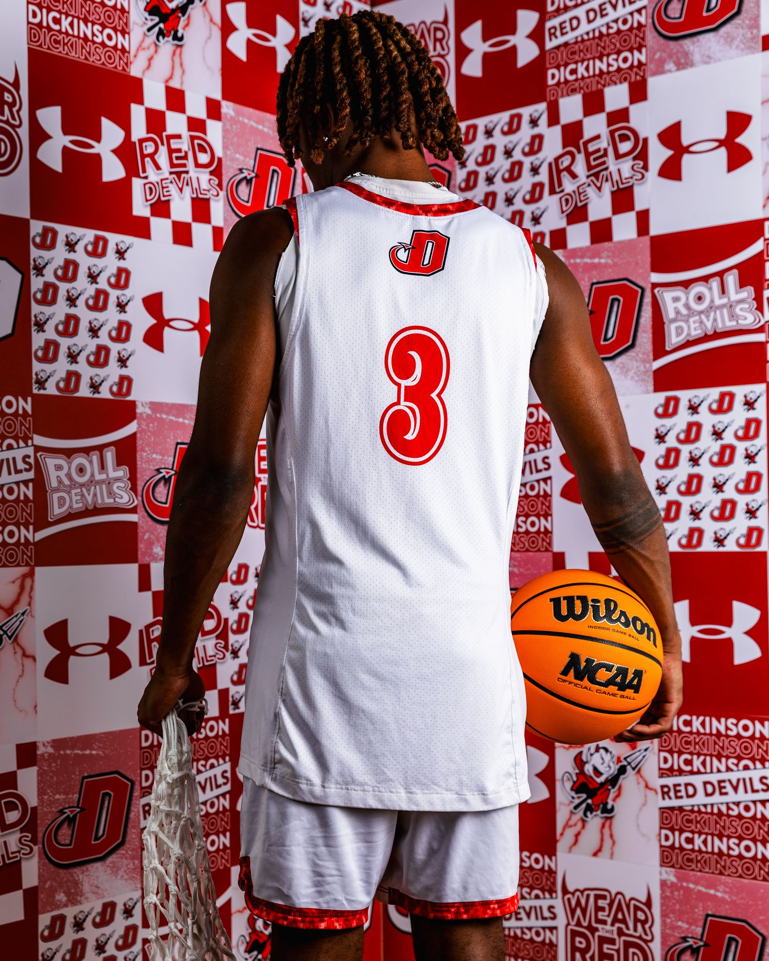 Basketball player in white jersey number 3 poses with ball against red and white Under Armour branded backdrop.